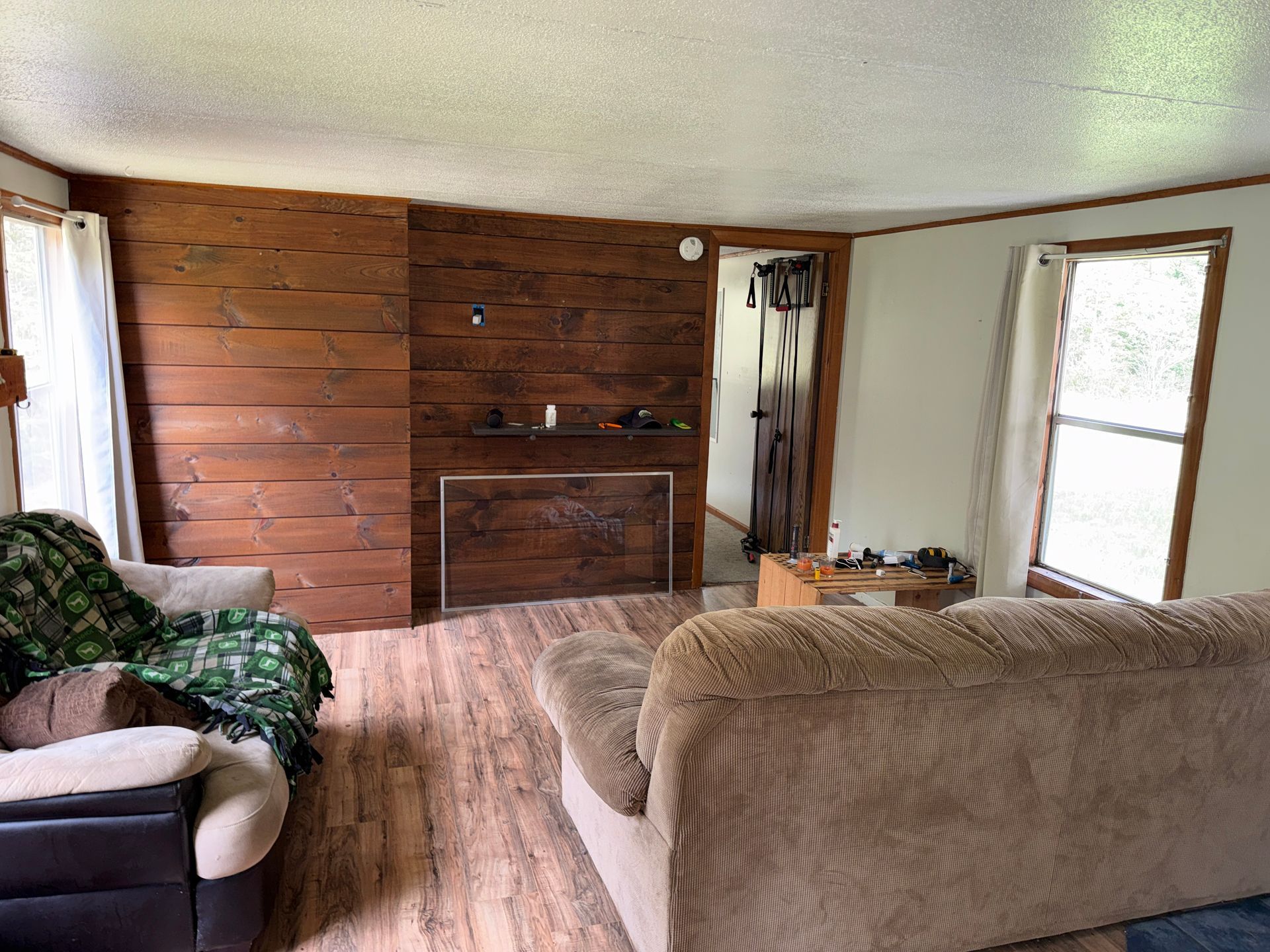 Cozy living room with wood-paneled wall, beige couch, armchair, and bright windows