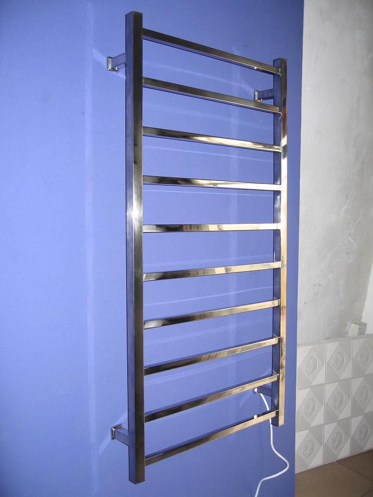Chrome towel warmer mounted on a blue wall; electric cord visible.