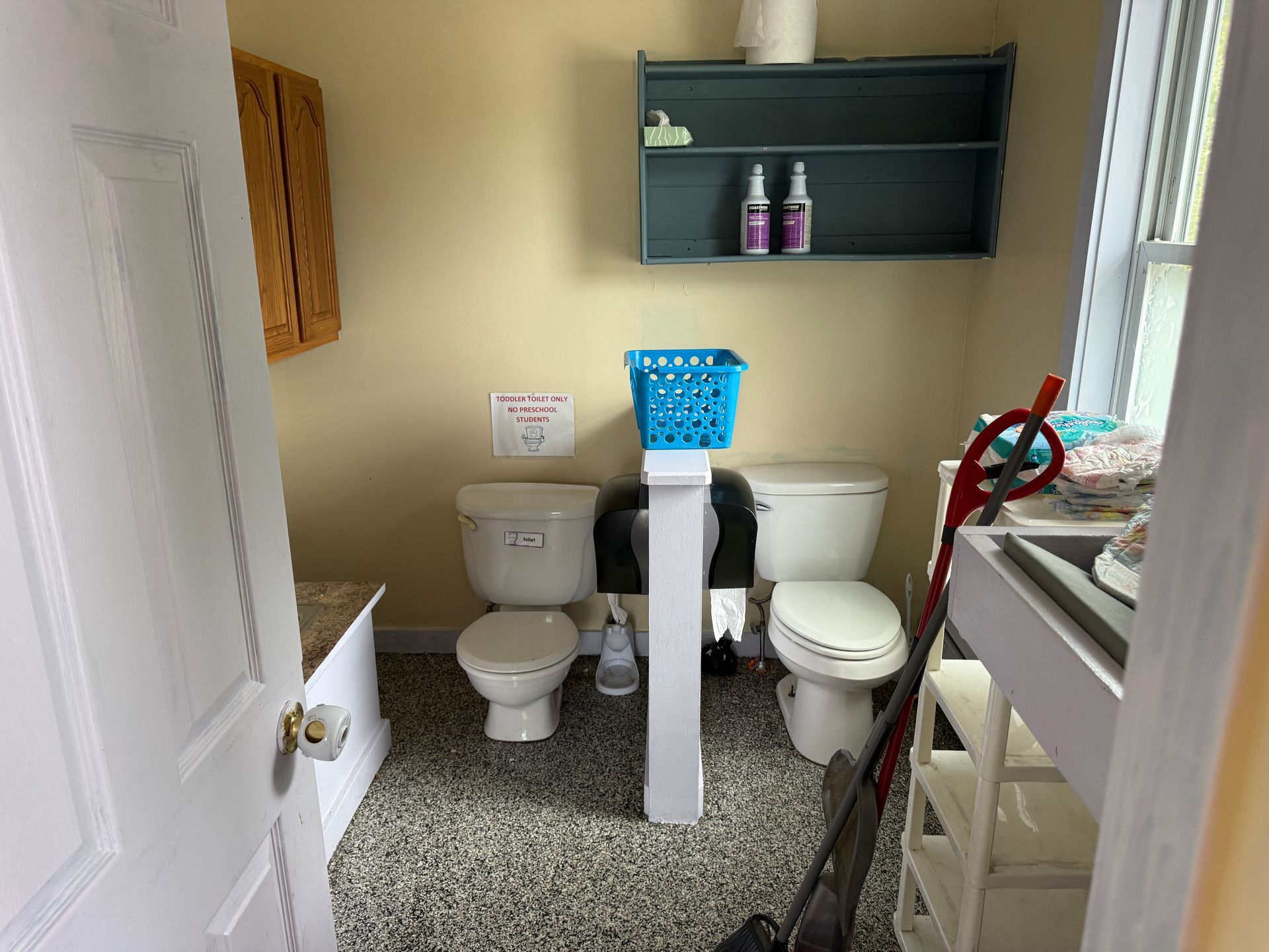 Small bathroom with a toilet, sink, shelves, and cleaning supplies; white and gray decor.