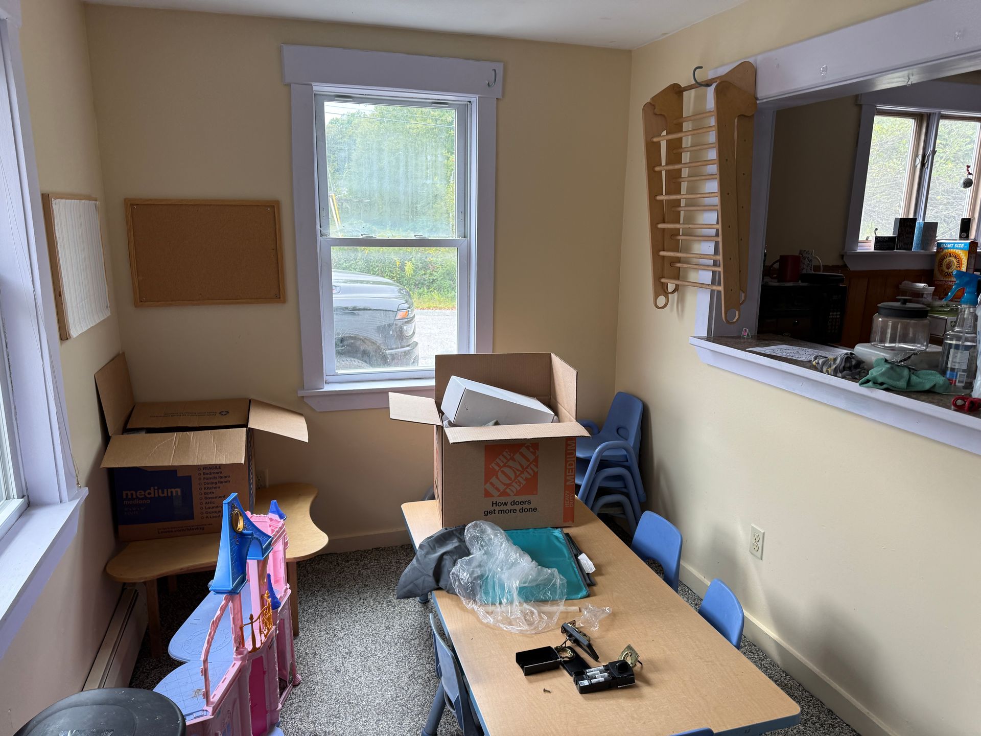 Small room with moving boxes, a table, window, and a pass-through to a kitchen area