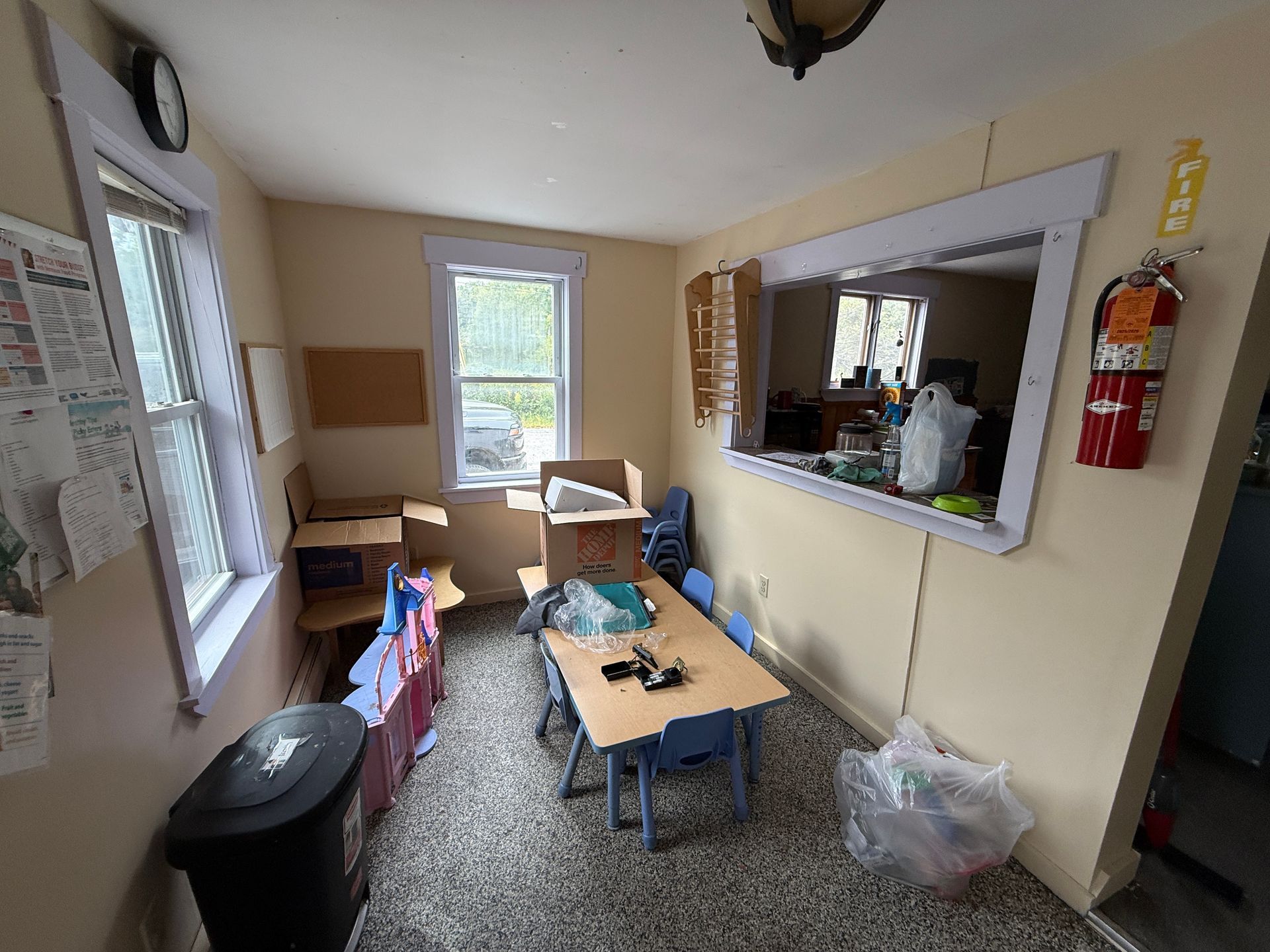 Small room with tables, chairs, windows, wall mirror, and a fire extinguisher.