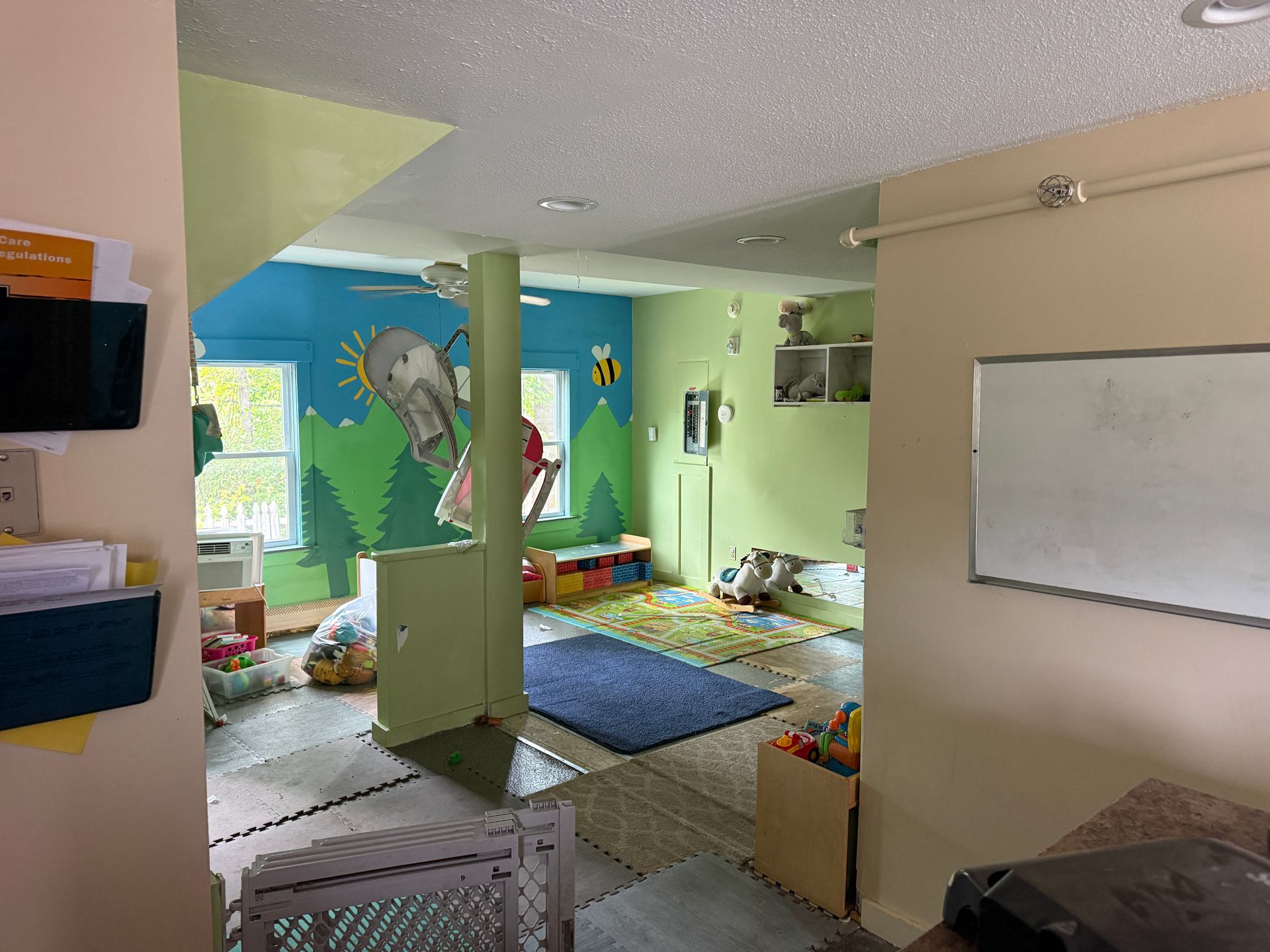 Colorful classroom with green walls, rugs, toys, whiteboard, and animal murals in a play area
