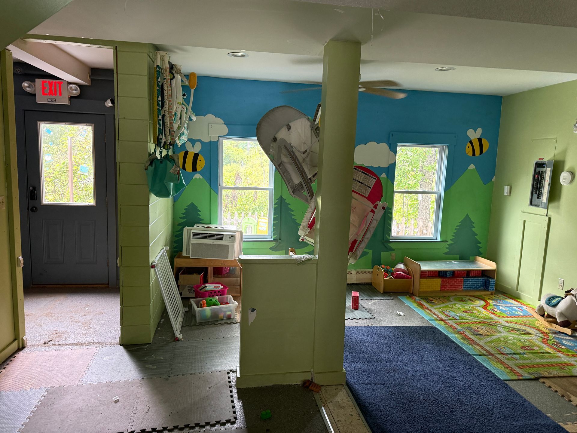 Bright kids’ playroom with green walls, blue rug, windows, toys, and wall art