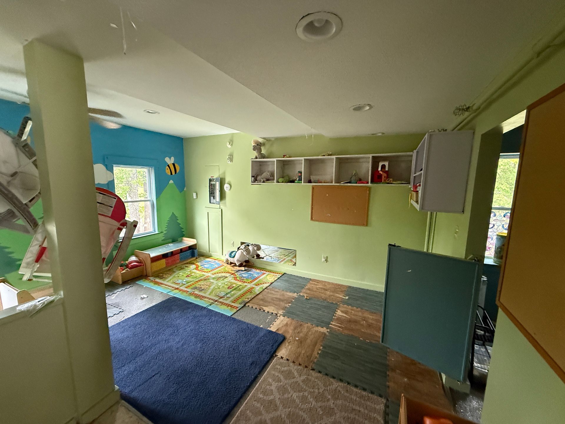Colorful classroom play area with rugs, shelves, windows, and a small table by the wall