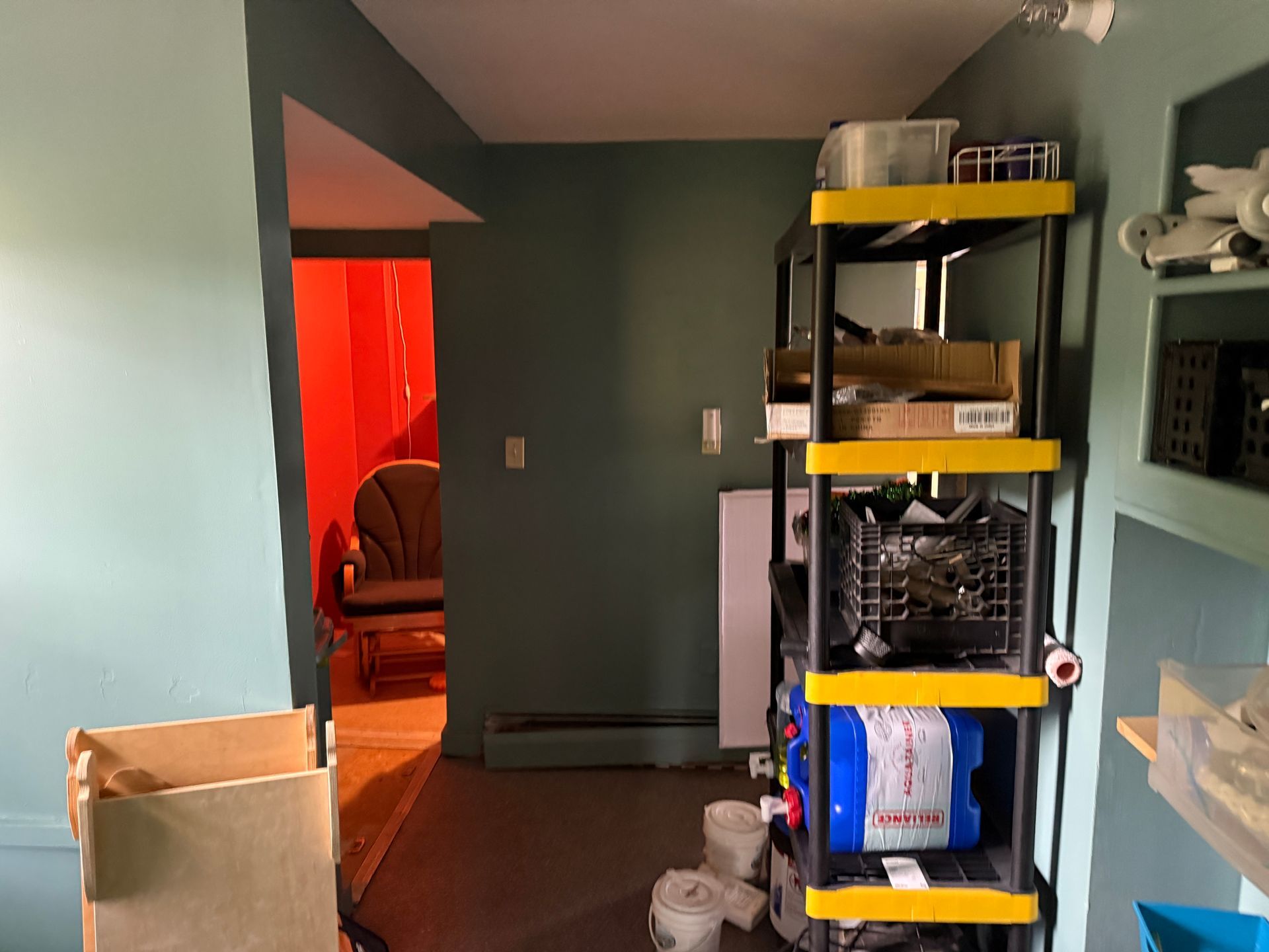 room with green walls, a black-and-yellow shelving unit, and a doorway lit by red light.