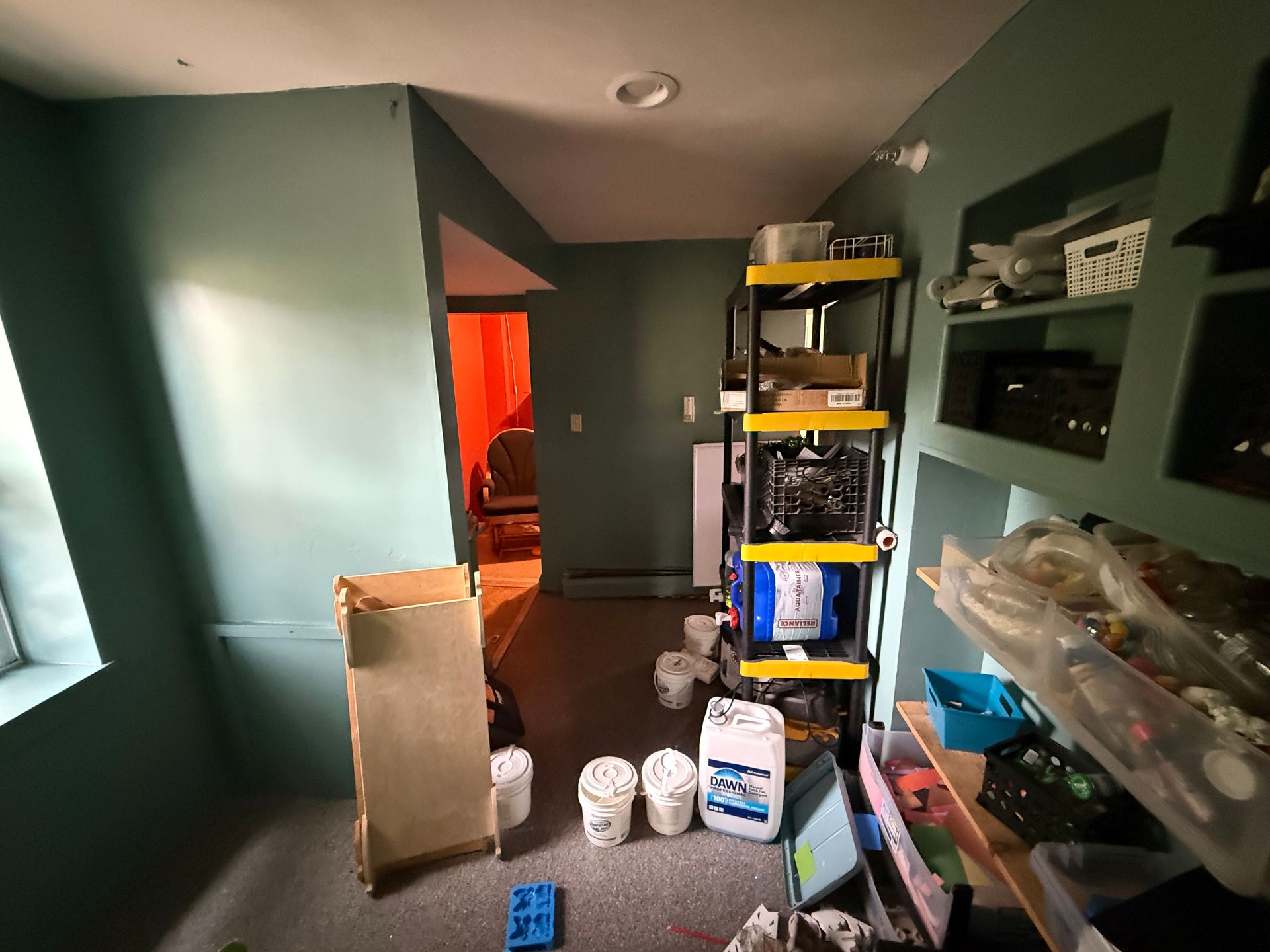 room with green walls, shelving, boxes, and supplies near an open doorway with orange light.