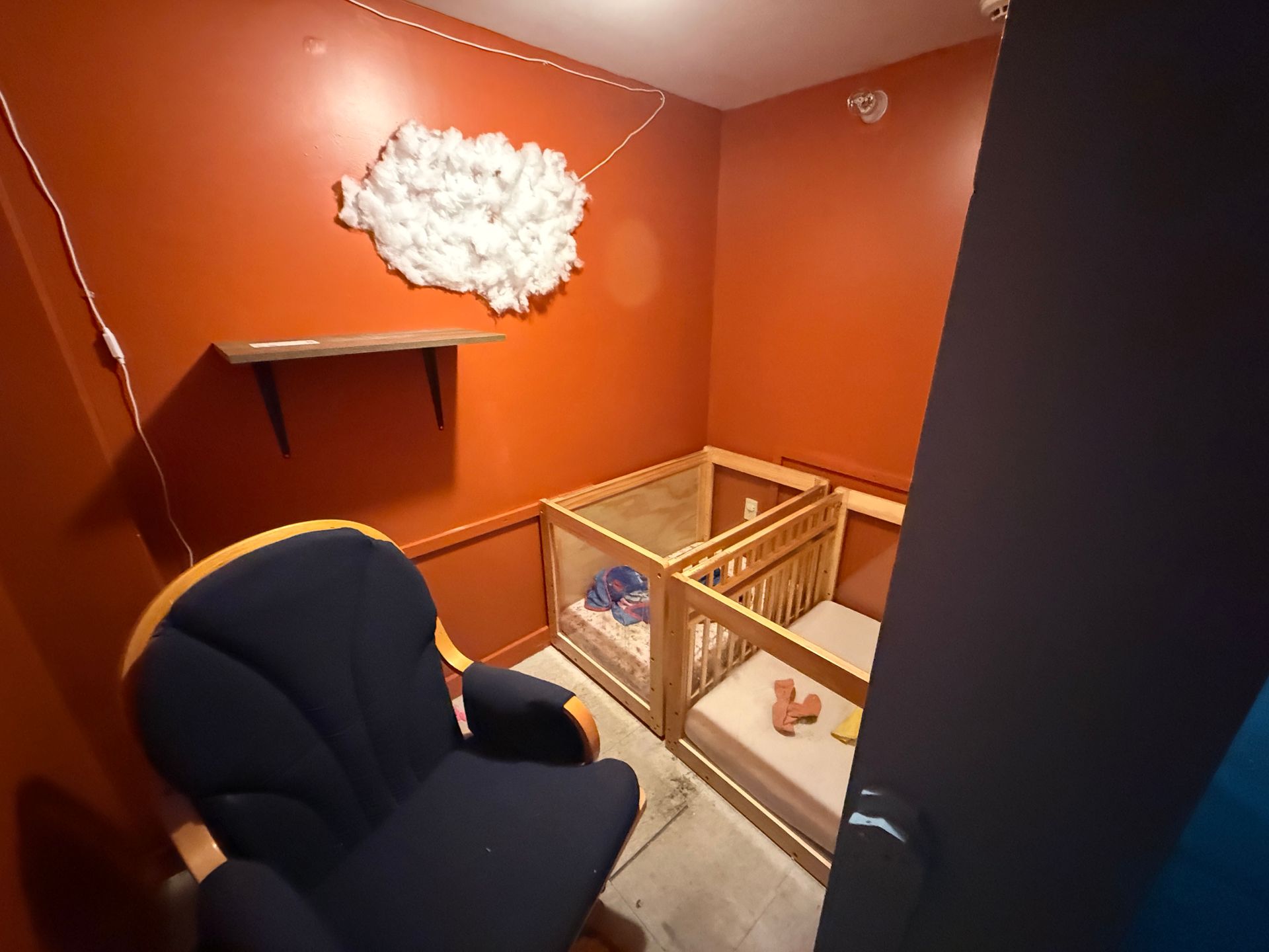 Orange nursery room with crib, navy chair, and white cloud wall decoration