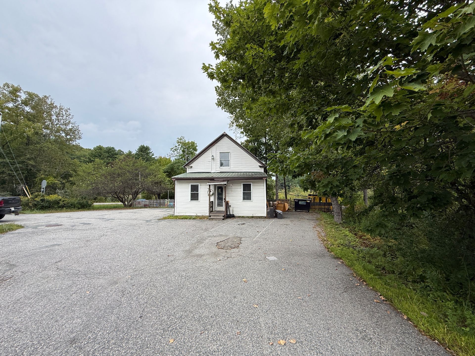 Small white house with a gravel driveway, surrounded by trees on an overcast day