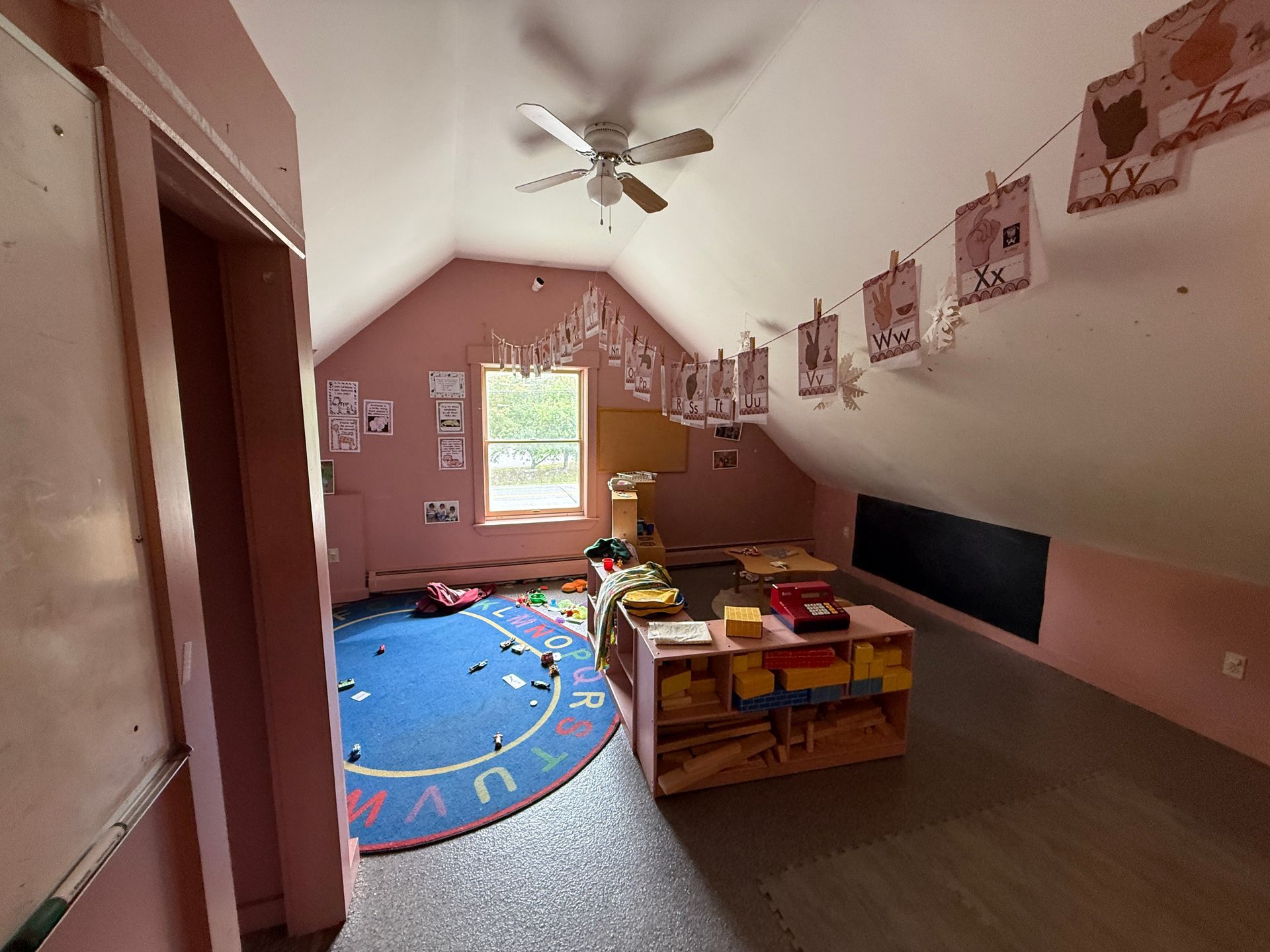 Attic playroom with blue rug, toy storage, and a ceiling fan under a sloped ceiling.
