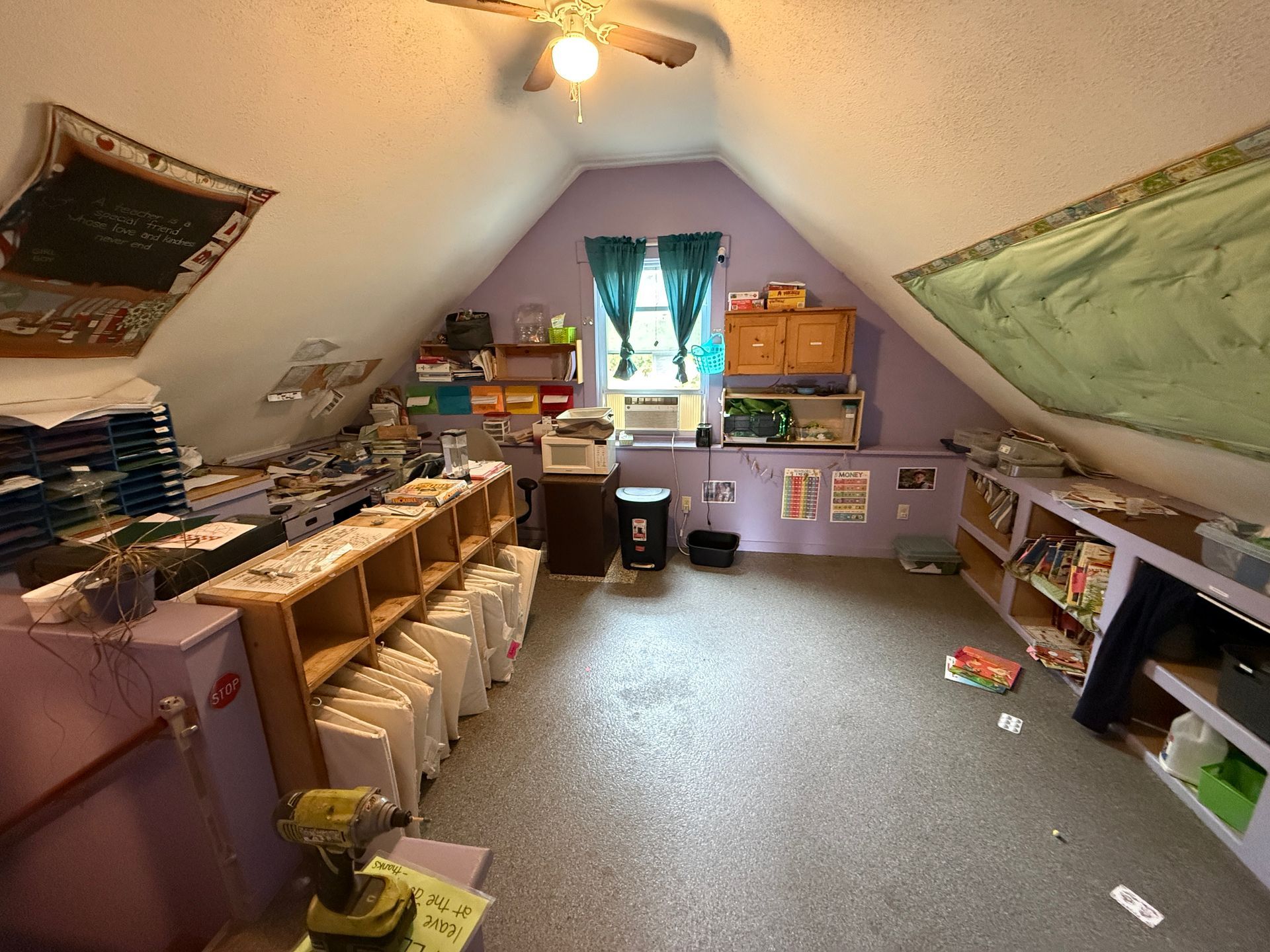 Attic room with shelves, bins, and storage boxes under a sloped ceiling, lit by a window and ceiling light