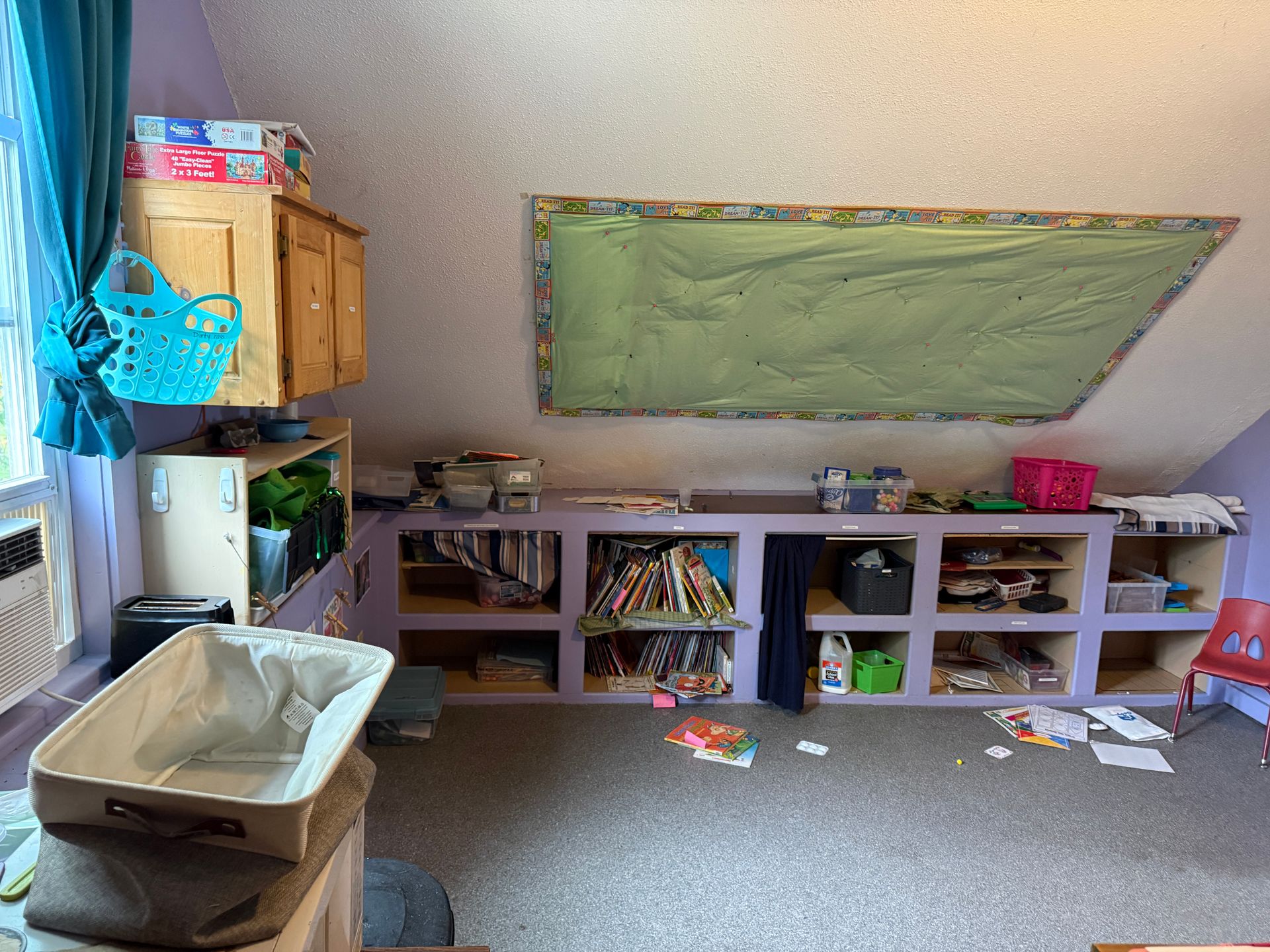 Kids' playroom with toy storage cubbies, bins, and a green wall board under a sloped ceiling