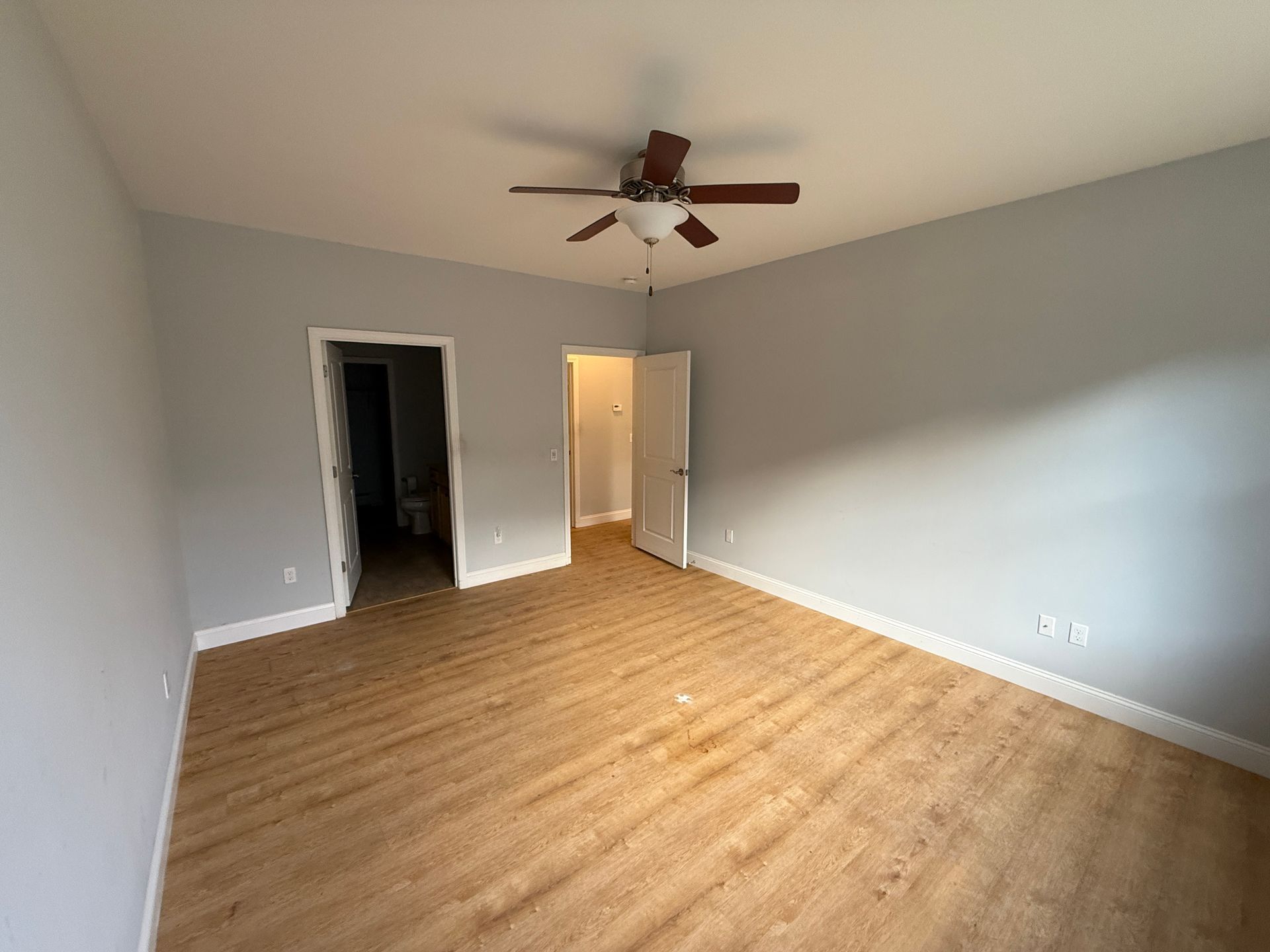 Empty bedroom with wood floors, white walls, ceiling fan, and two doorways.