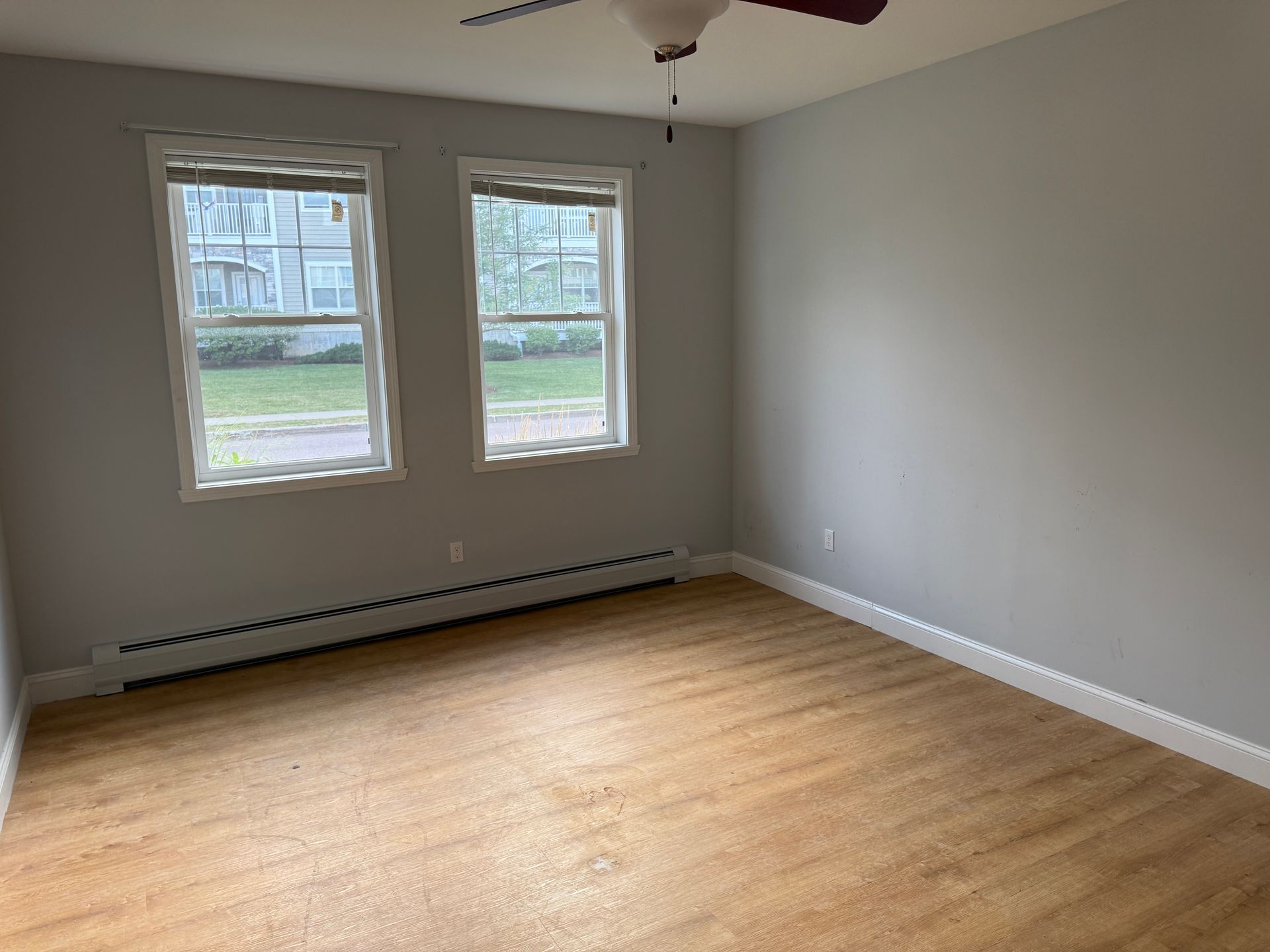 Empty gray bedroom with hardwood floor and two windows