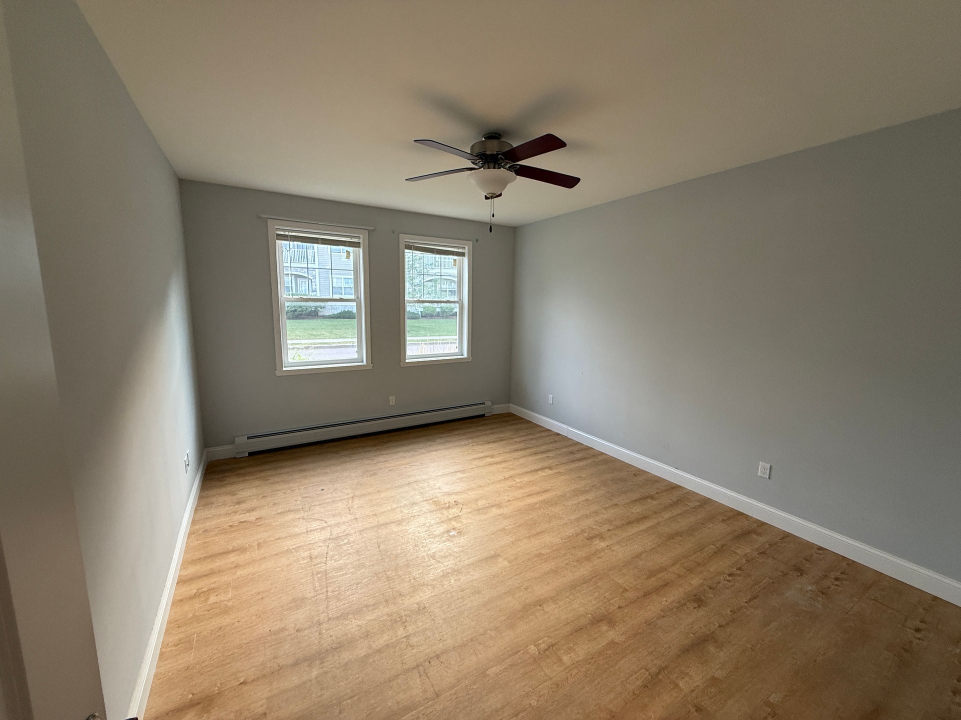 Empty gray bedroom with wood floors, two windows, and a ceiling fan.