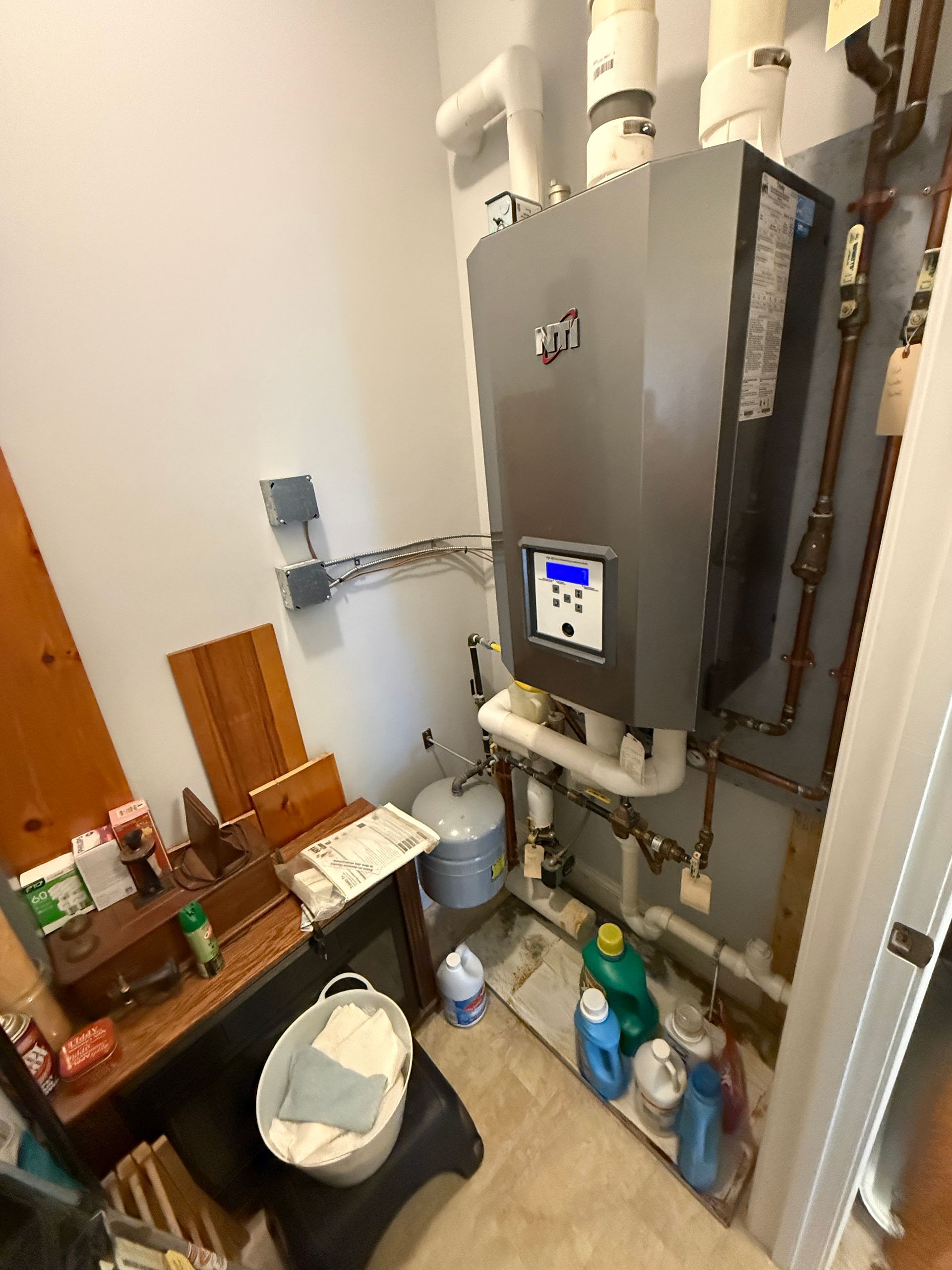 Utility closet with a wall-mounted water heater, shelves of cleaning supplies, and a laundry basket