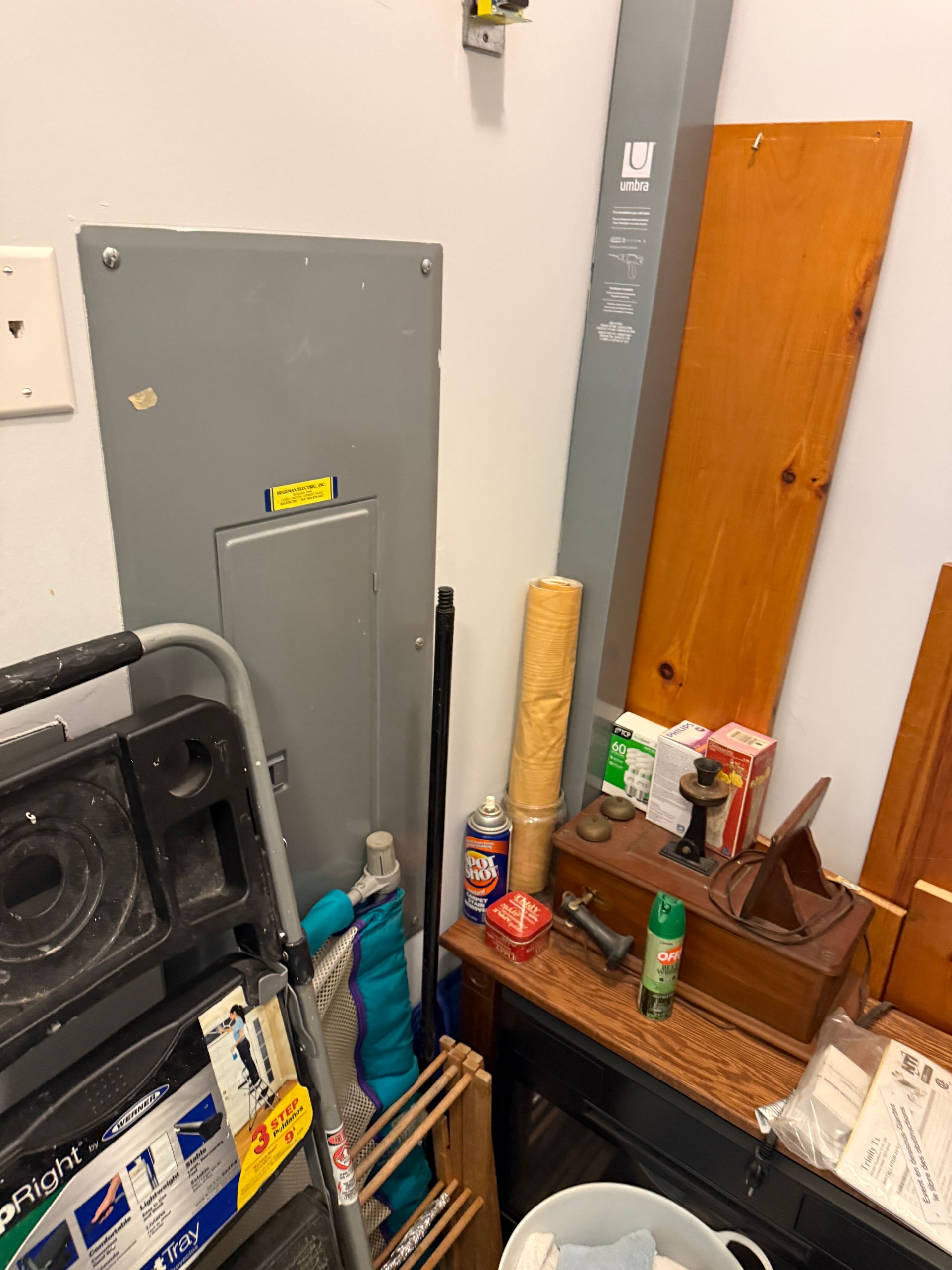 Storage area with gray electrical panel, open case, and assorted tools and items stacked on a shelf.