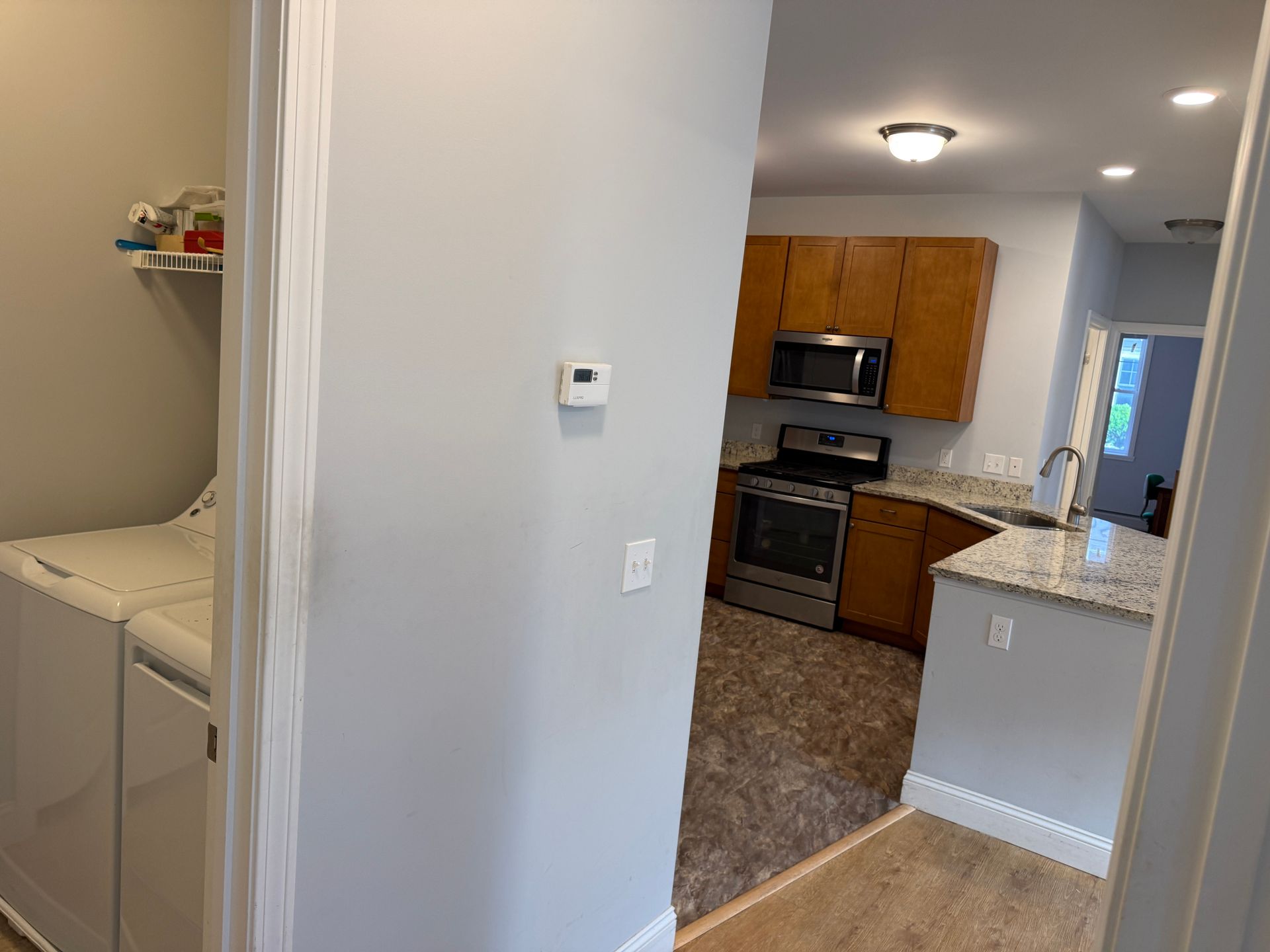 View from hallway into kitchen with granite counters, stainless appliances, and laundry nook on the left