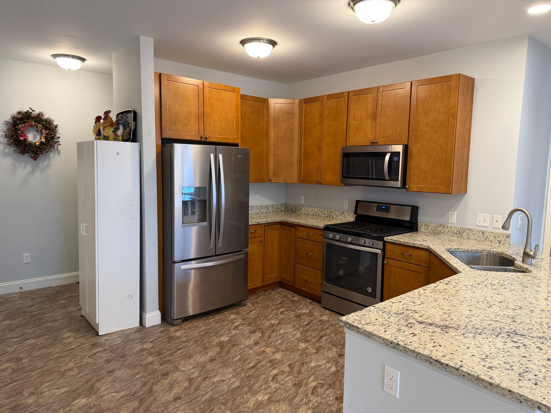 Modern kitchen with stainless steel appliances, wood cabinets, and speckled granite countertops