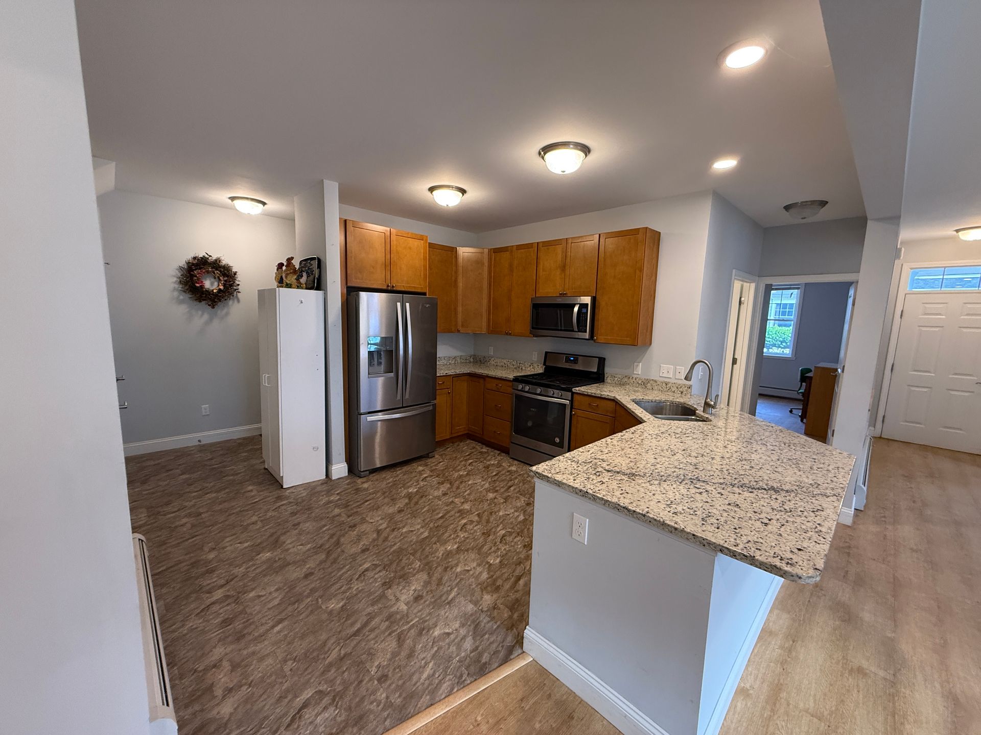 Empty kitchen with stainless steel appliances, granite counter, and brown carpeted living area.