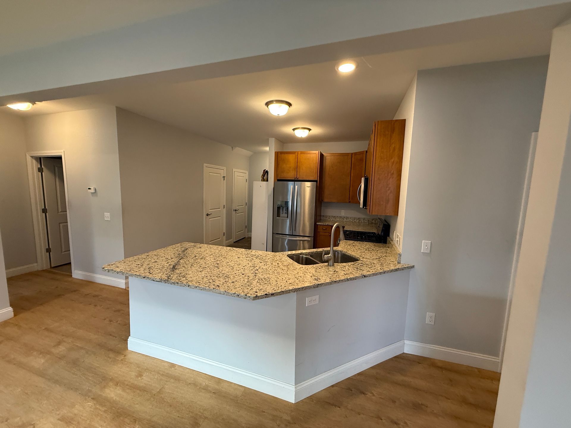 Open kitchen with granite island, stainless refrigerator, wood cabinets, and recessed lighting in a beige room
