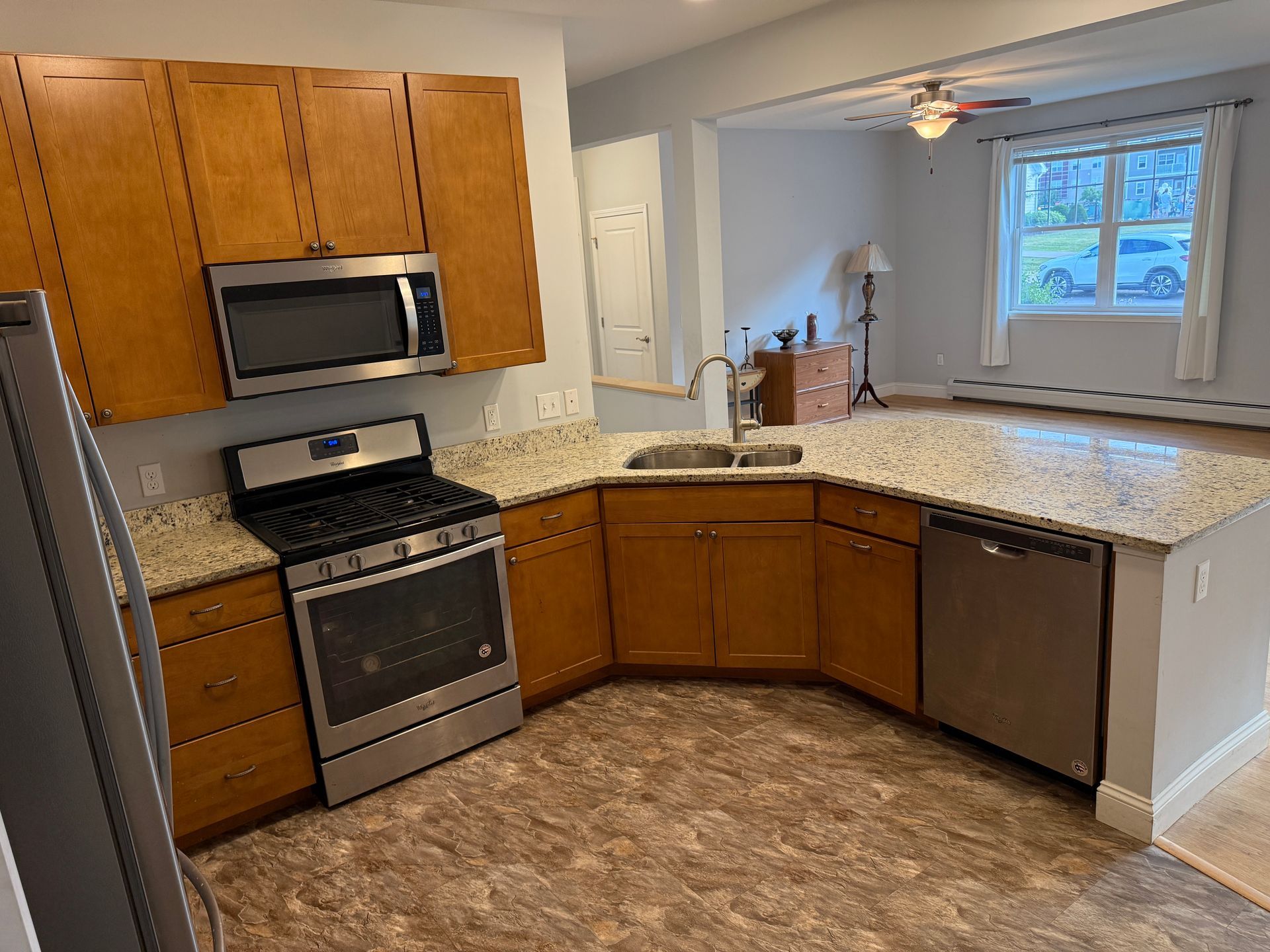 Empty kitchen with wood cabinets, stainless appliances, and beige speckled counters and floor.