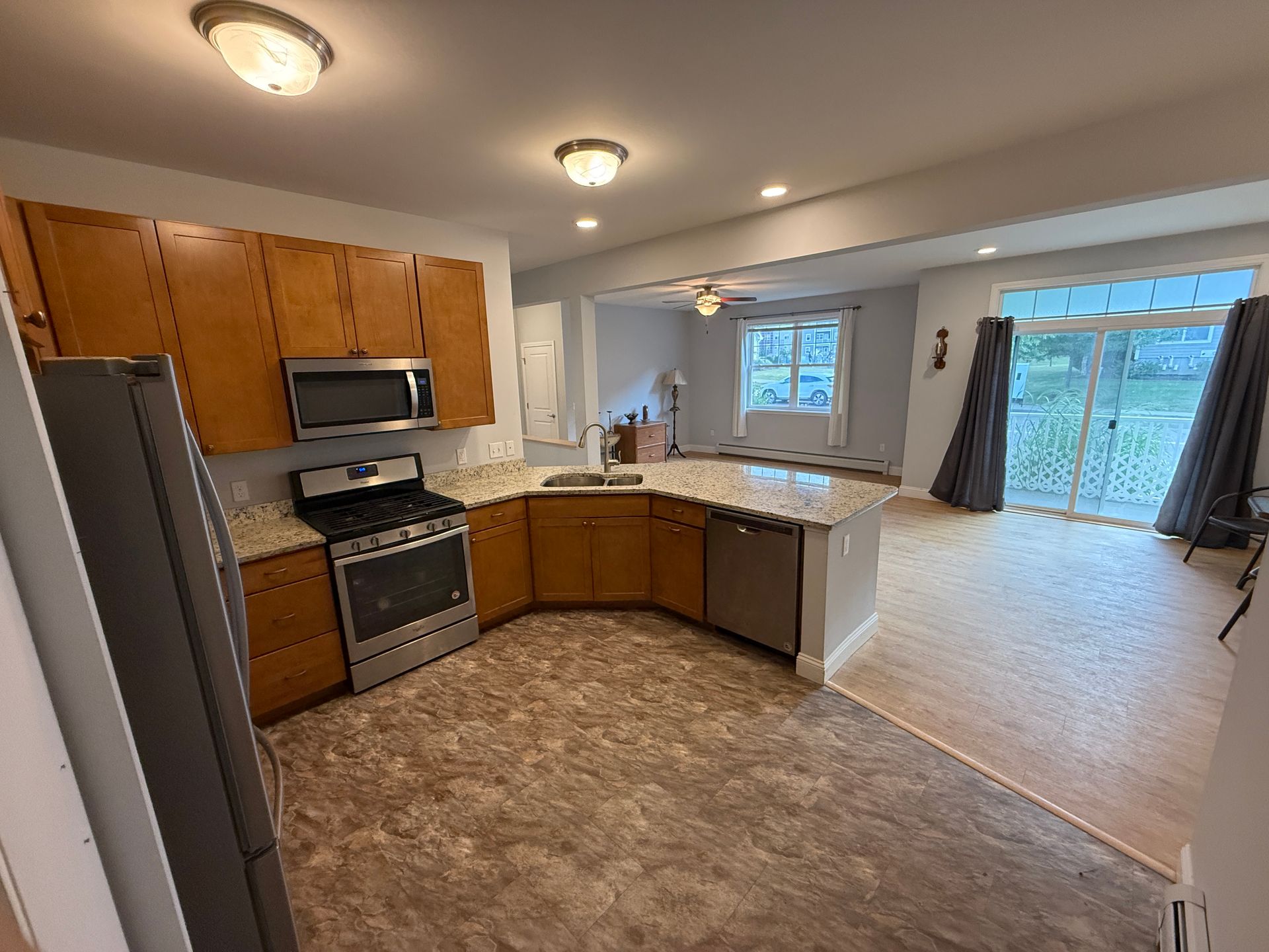 Empty kitchen and dining area with wood cabinets, stainless appliances, and sliding glass doors.