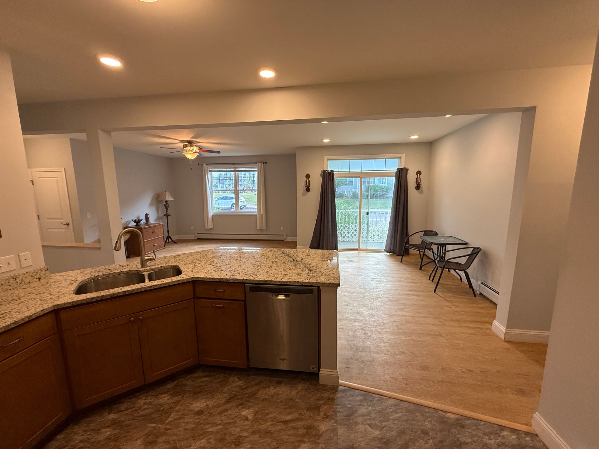 Open kitchen with granite counters, wood cabinets, and a dining area leading to glass doors and a patio.