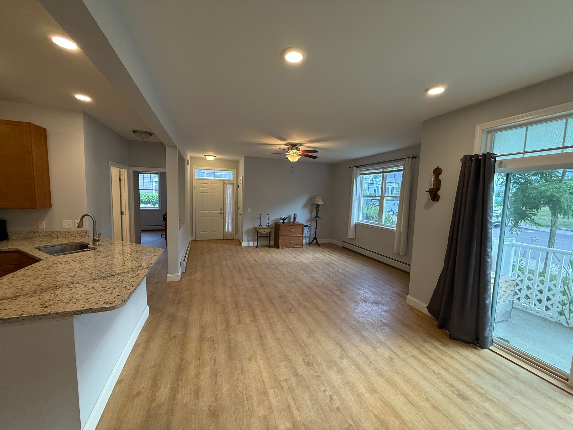 Empty open-concept living room with kitchen, hardwood floors, and sliding glass door to a patio.