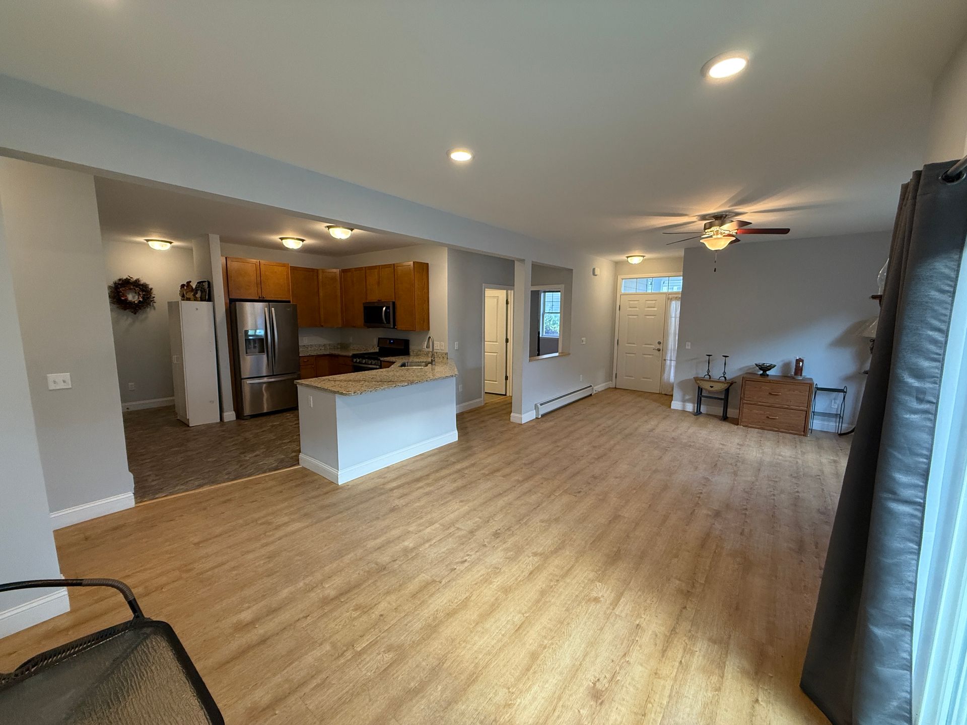 Empty open-plan living room with hardwood floors, kitchen island, and a small dining area.