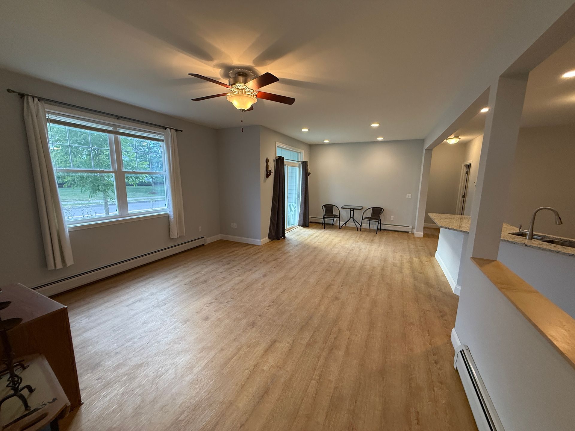 Empty open-plan living room with wood floors, recessed lights, ceiling fan, and large window.