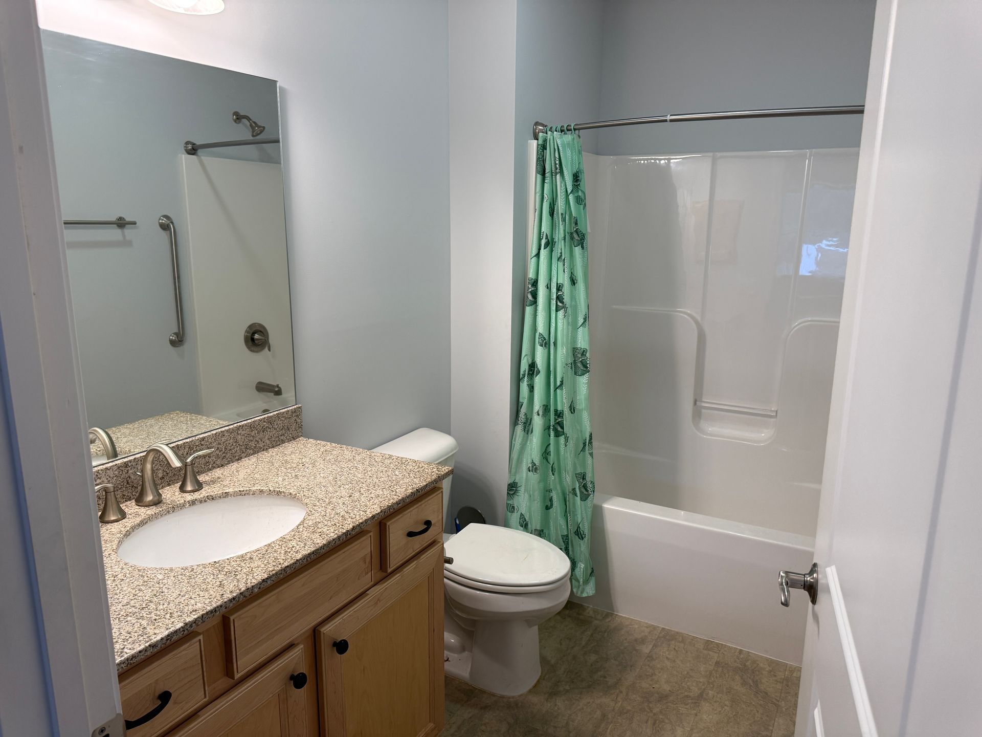 Small bathroom with vanity, mirror, toilet, and bathtub with green shower curtain.