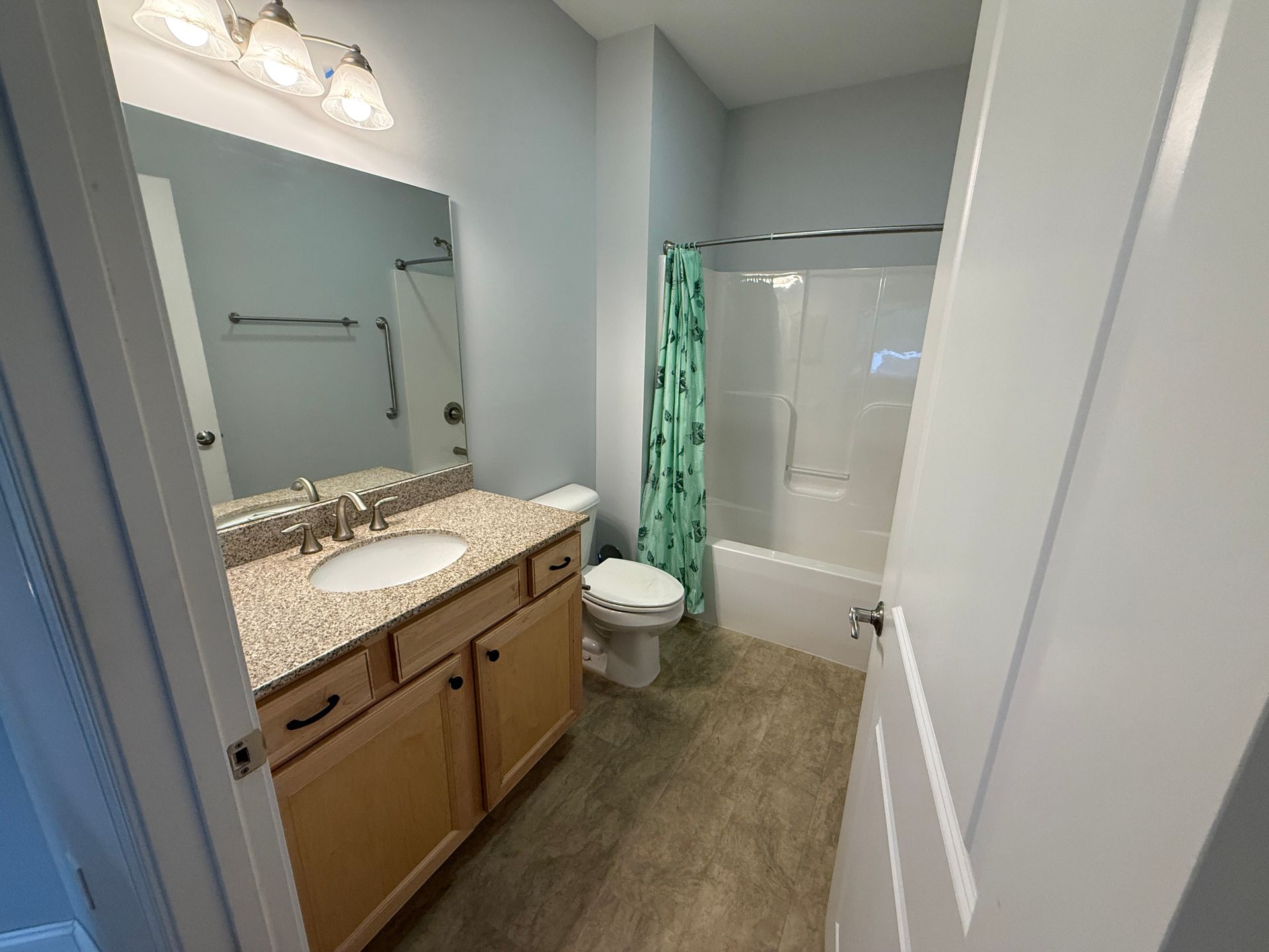 Small bathroom with vanity, large mirror, toilet, and shower with green curtain.