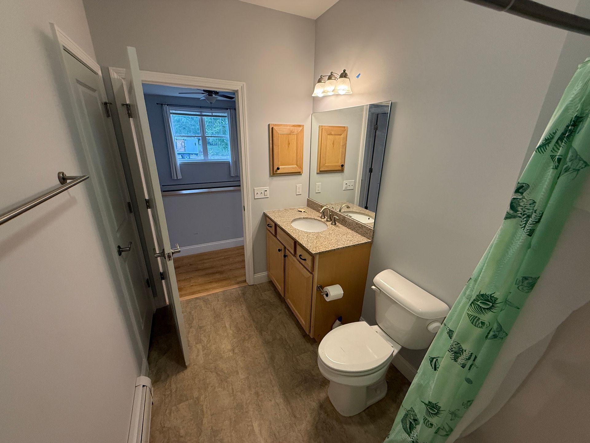 Narrow bathroom with wood-look floor, white toilet, sink cabinet, and shower curtain by the tub