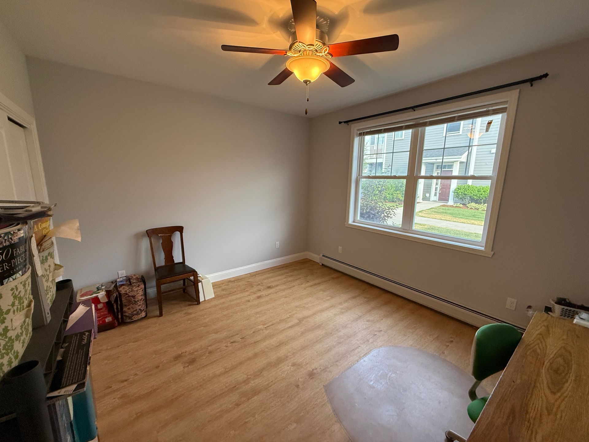 Empty living room with light wood floor, ceiling fan, large window