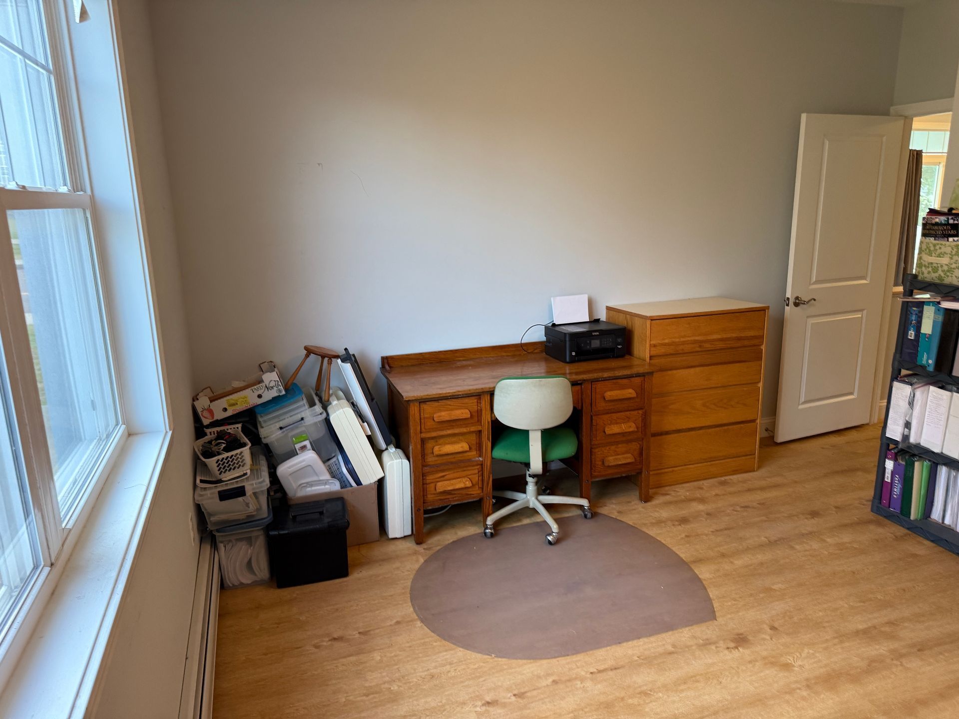 Home office with desk, stool, dresser, boxes, and large window on the left.