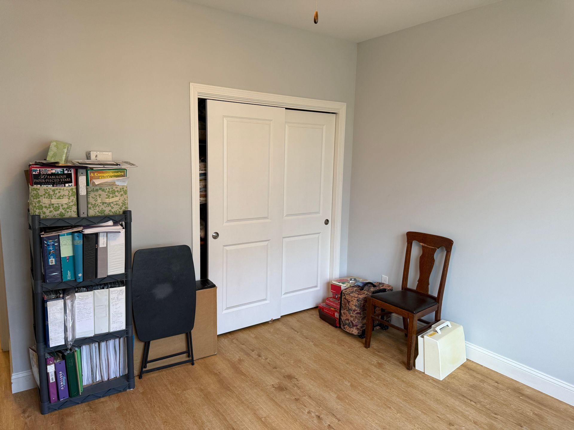 Small empty room with white double doors, a bookshelf, chair, and a few boxes on hardwood floor.