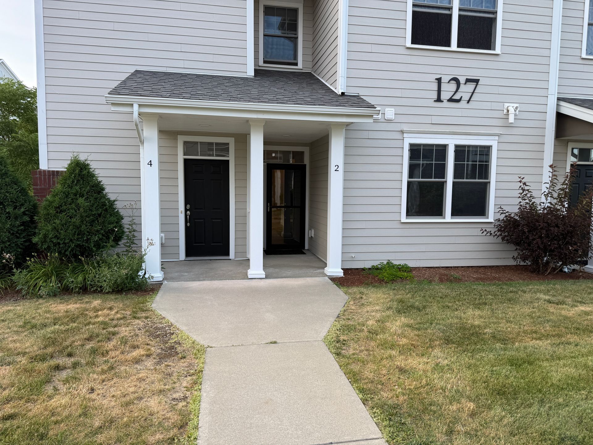 Apartment entrance with white siding, covered porch, and walkway leading to door number 127.