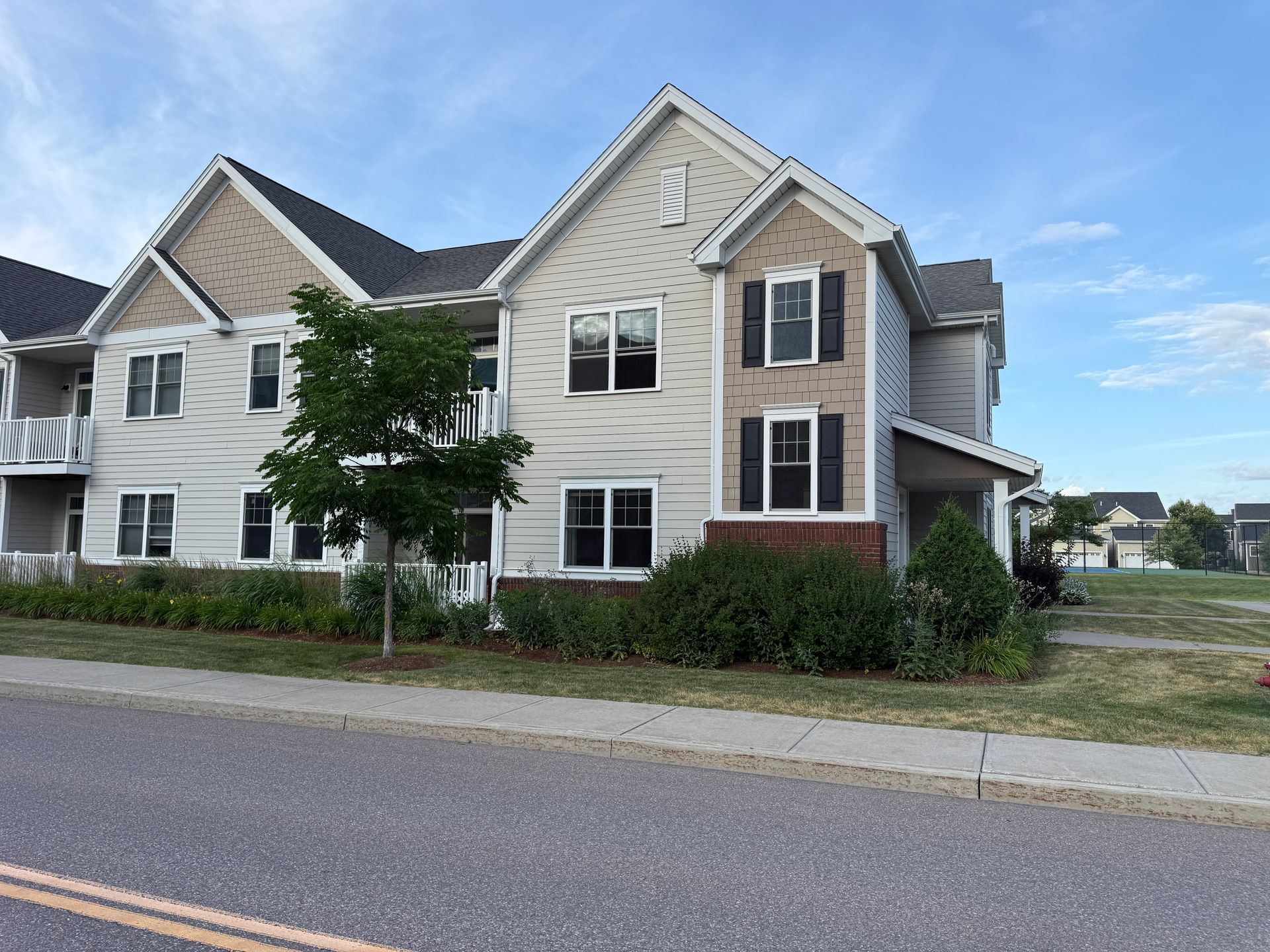 Apartment building with beige and white siding beside a road, under a partly cloudy sky