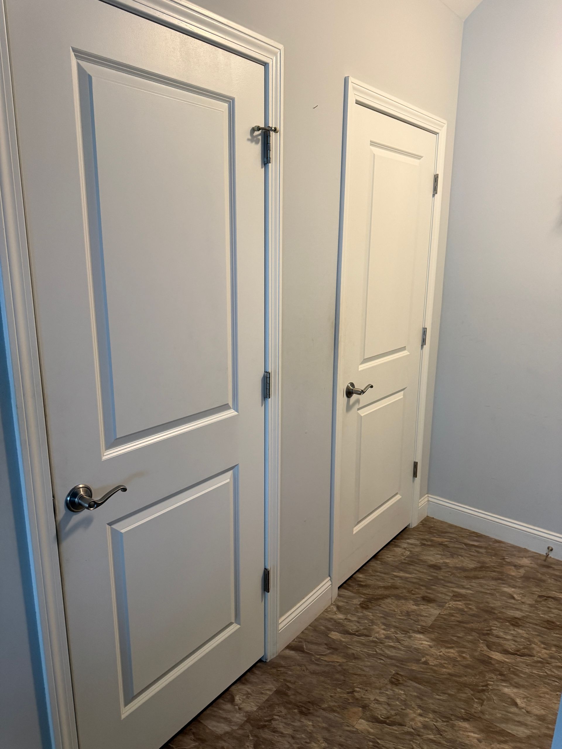 Two white interior doors in a carpeted hallway with light blue walls