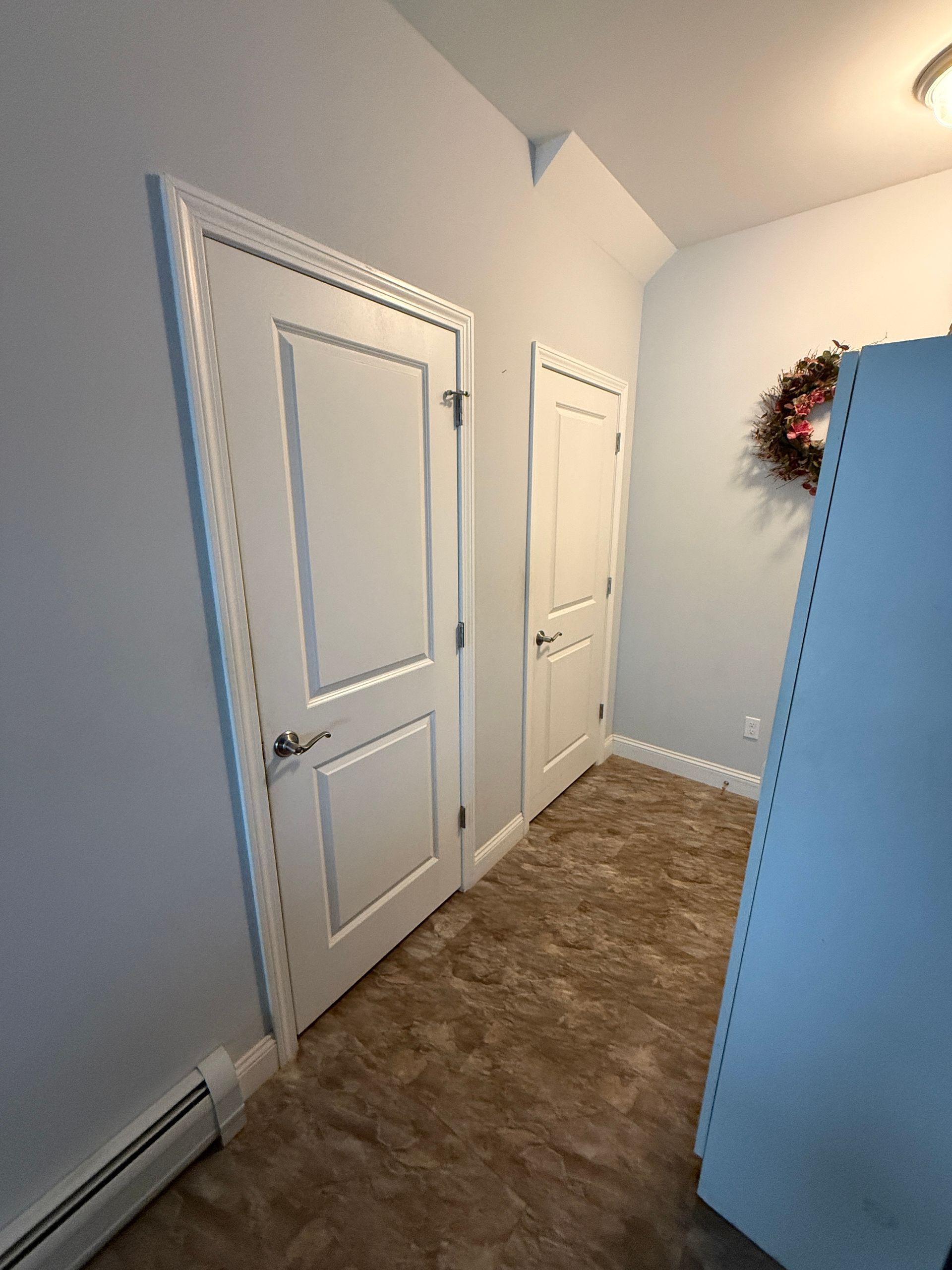 Narrow hallway with white doors, light blue walls, and brown carpet.