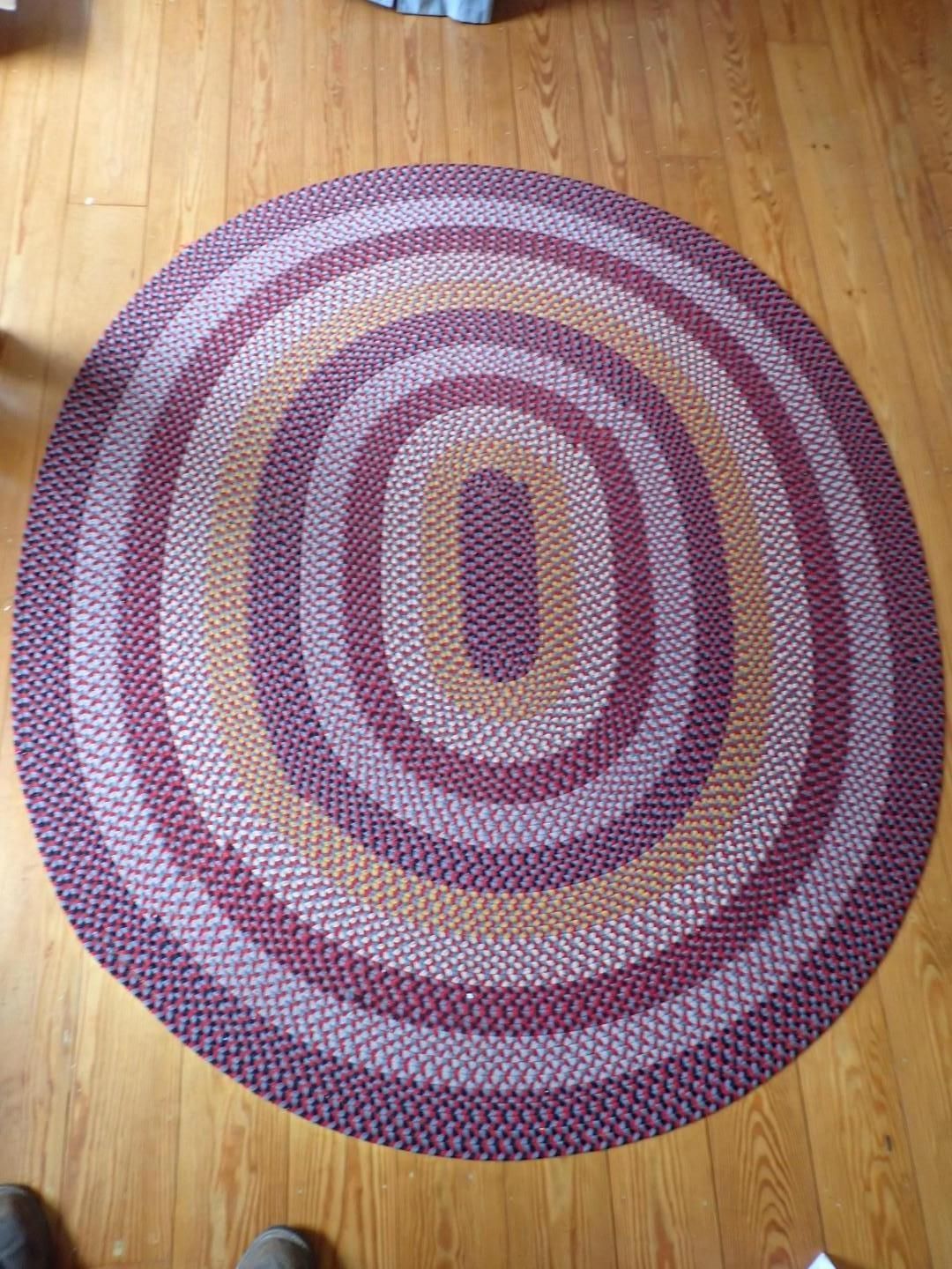 Oval braided rug with concentric rings in pink, purple, and cream on a wooden floor