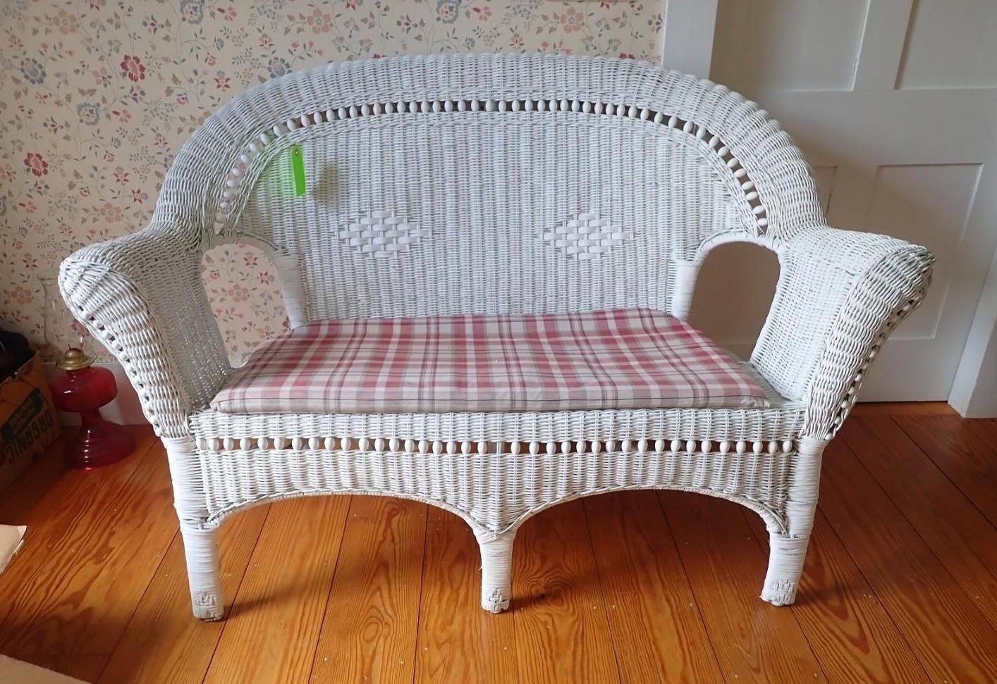 White wicker loveseat with pink cushion on a hardwood floor against a floral wallpapered wall