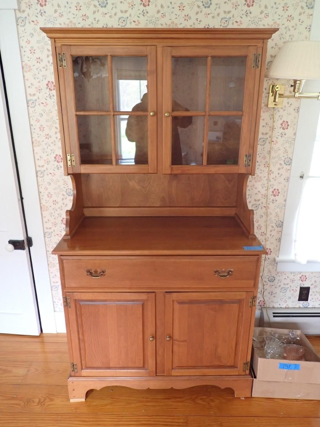 Wooden hutch cabinet with glass doors and drawers against floral wallpaper in a room
