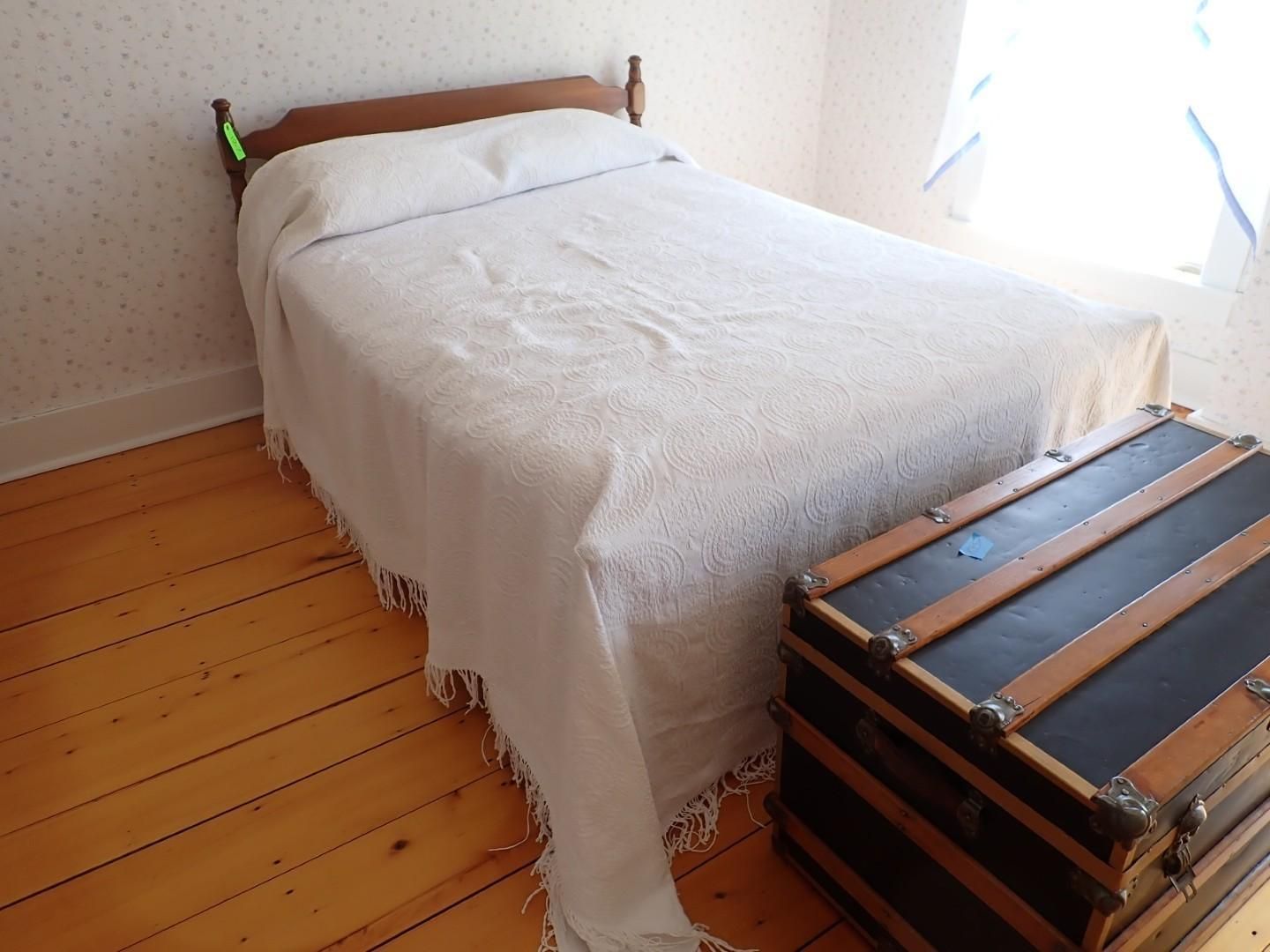 White bed in a sunlit room with wooden floor and a trunk at the foot of the bed
