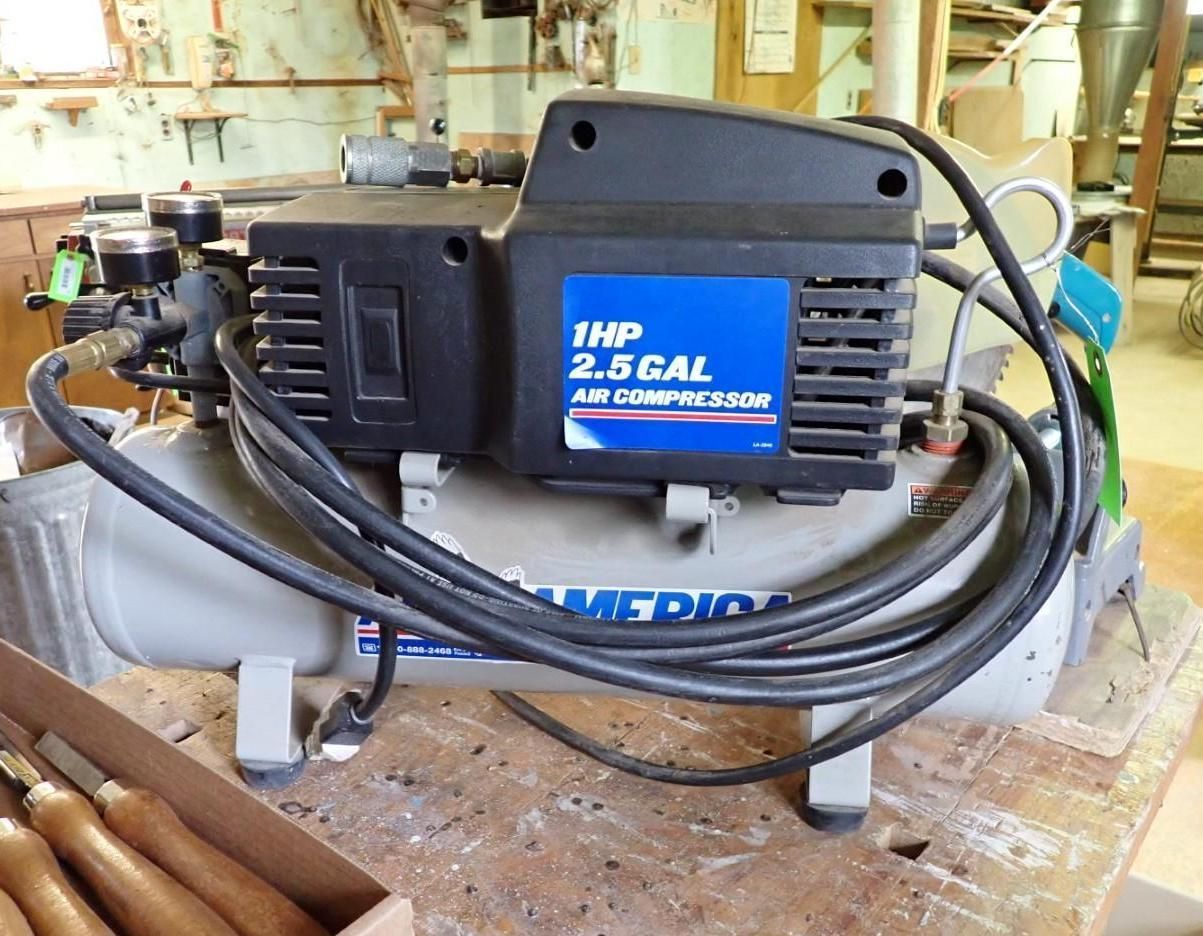 Black air compressor with coiled hose on a worn workbench in a workshop