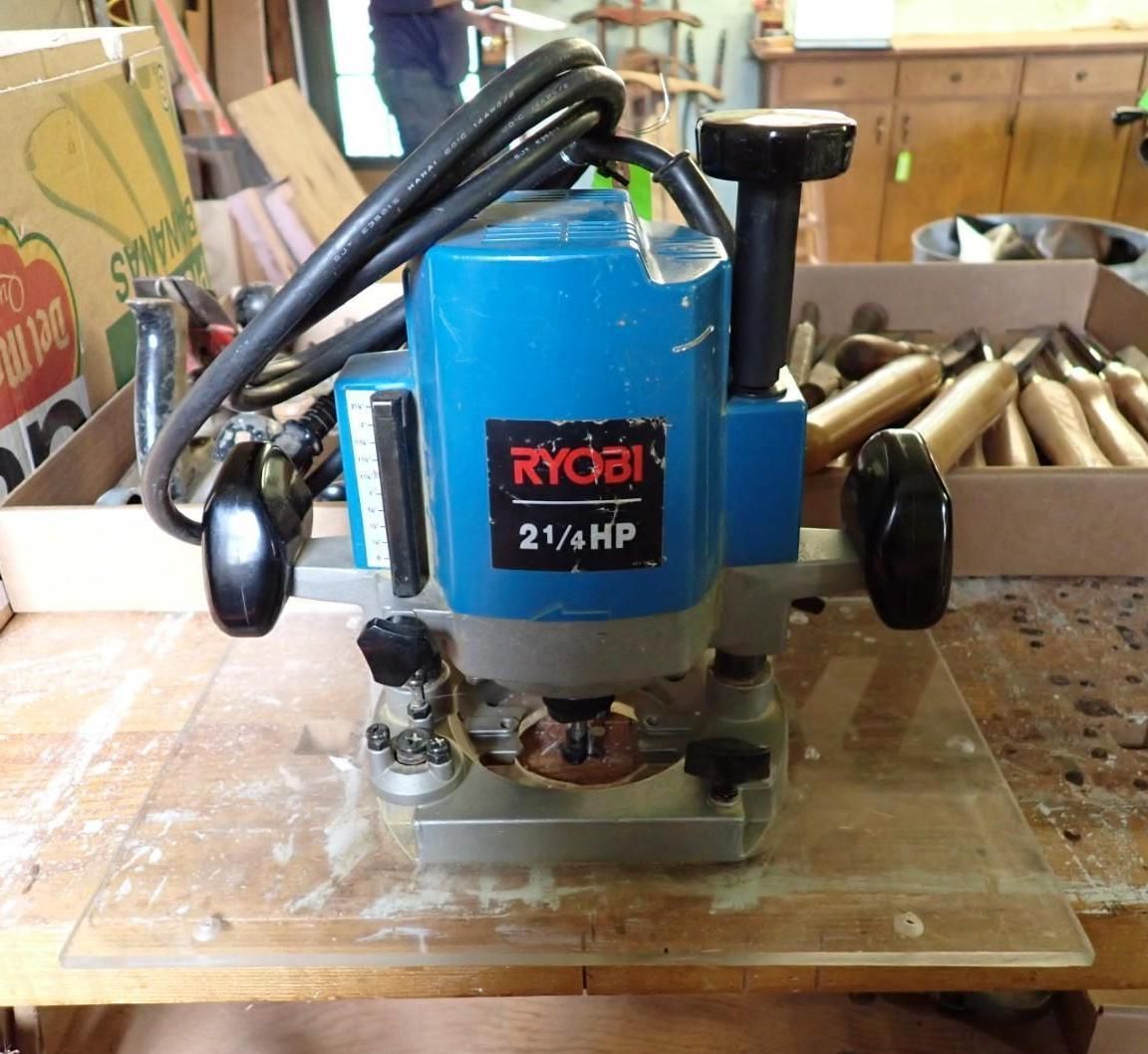 Blue Ryobi 2 1/4 HP router on a workbench, with black handles and power cord attached