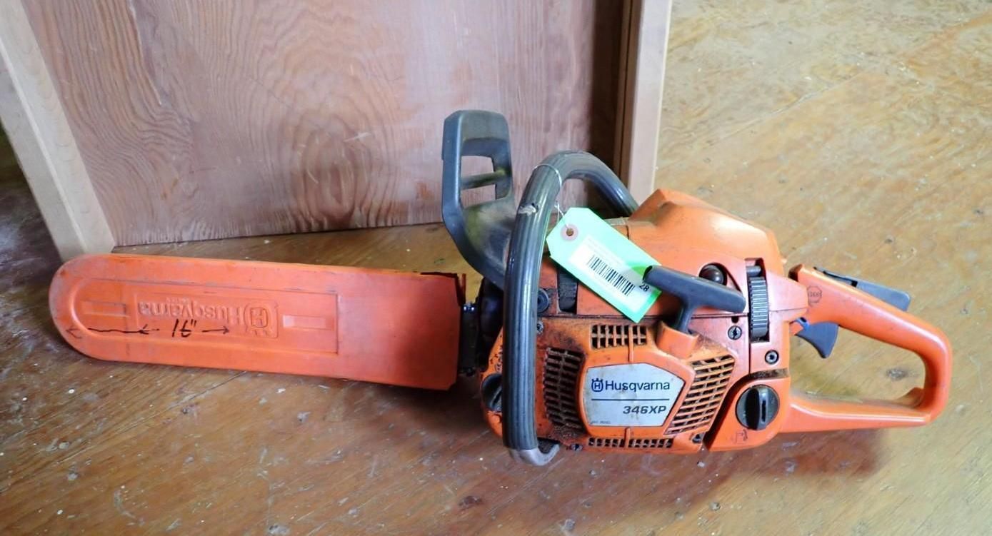 Orange chainsaw resting on a wooden floor beside a wall