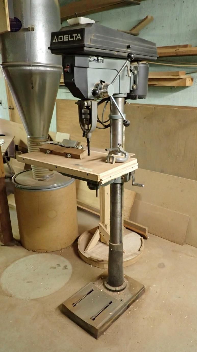 Workshop floor drill press with a metal cone hopper and small worktable on a stand.