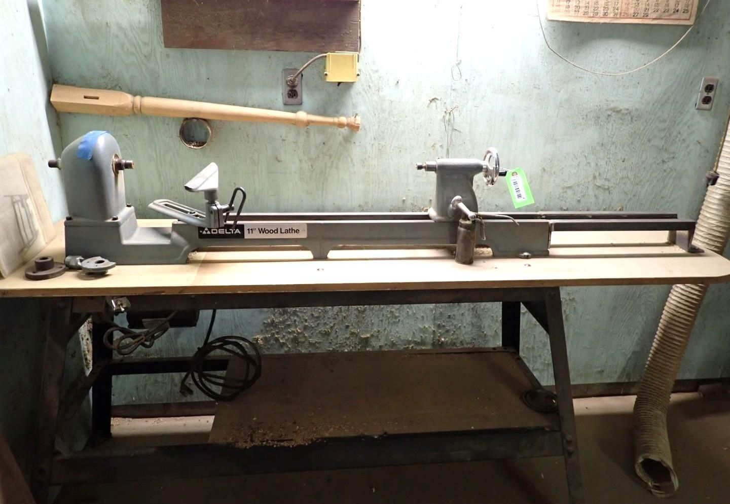 Woodworking lathe on a bench in a workshop, with tools and a dust hose underneath.