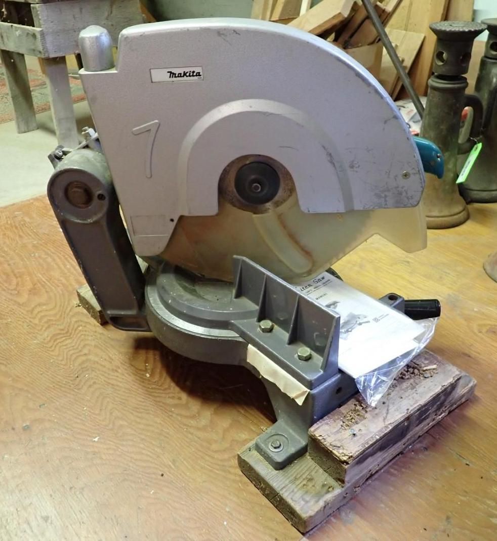 Metal-cutting chop saw on a workbench, with a blade guard and clamped metal piece.